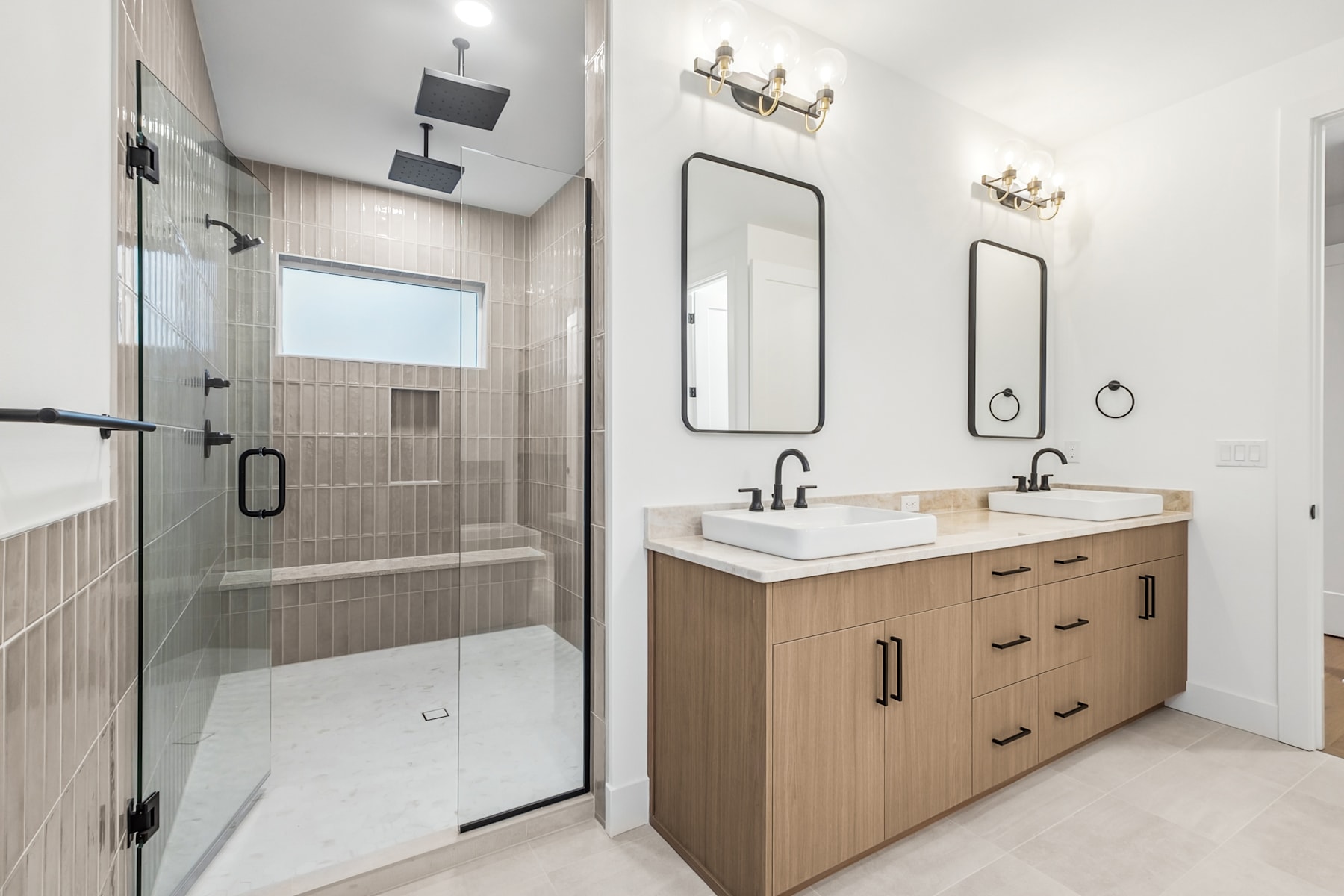 A modern and well-designed bathroom with a glass shower enclosure, a vanity with dual sinks, and wall-mounted mirrors and lighting fixtures.