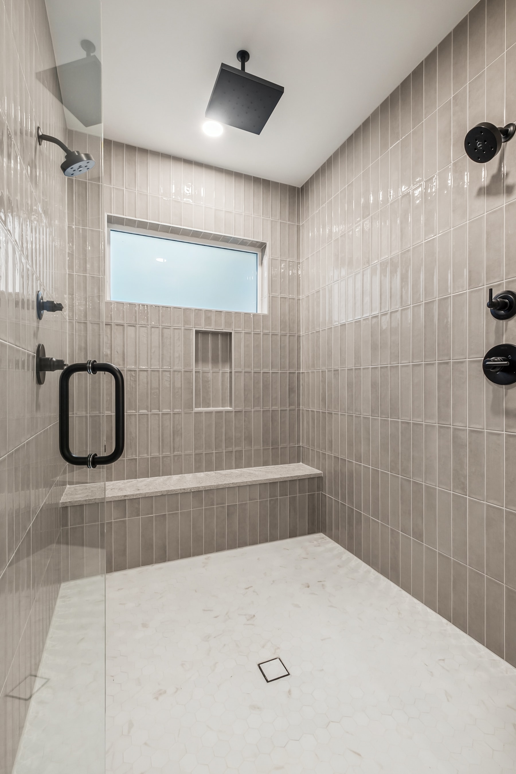 A spacious, tiled bathroom with a large shower area, a recessed ceiling light, and a window providing natural light.