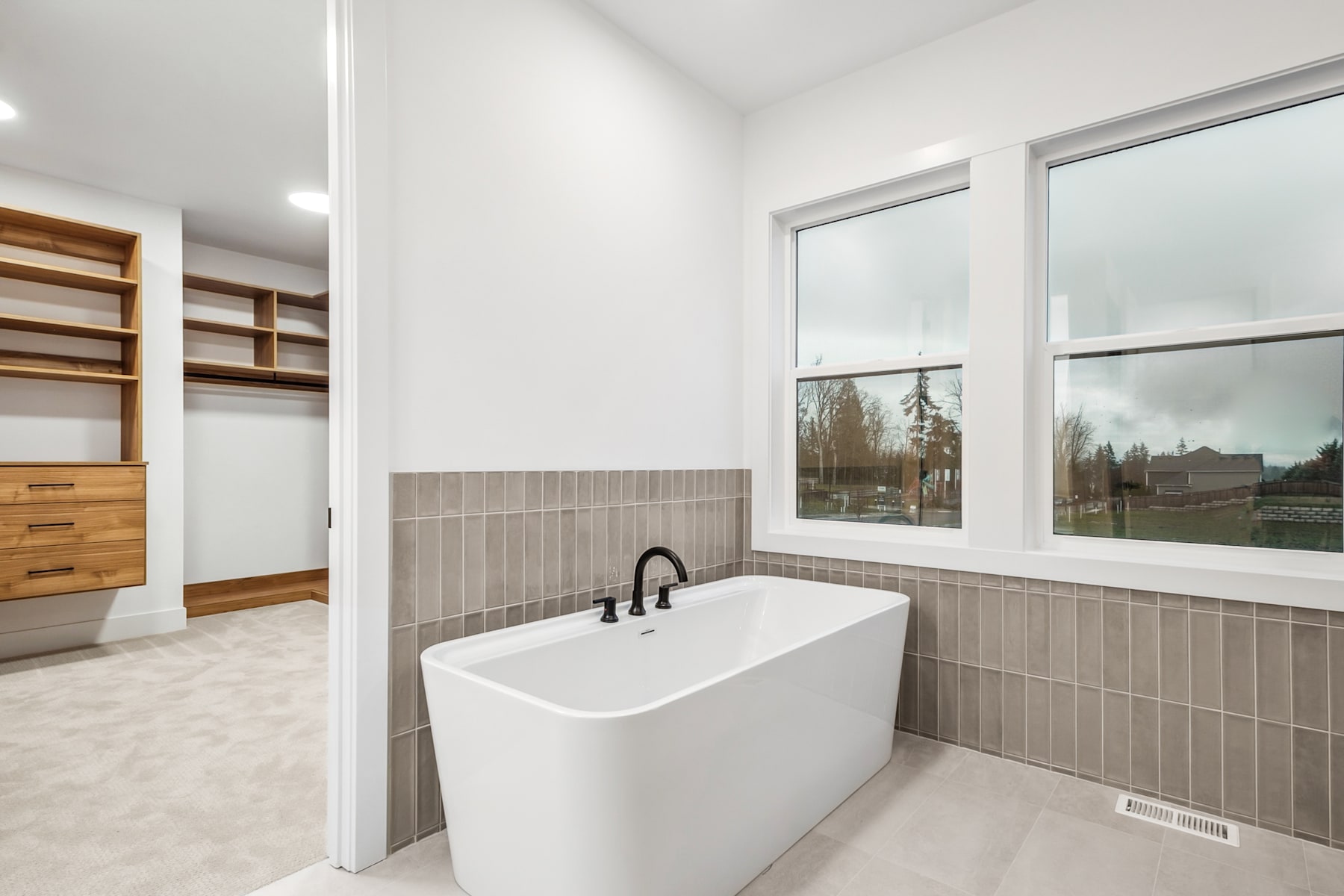 A modern and spacious bathroom with a freestanding bathtub, wooden shelves, and a large window overlooking a scenic outdoor landscape.