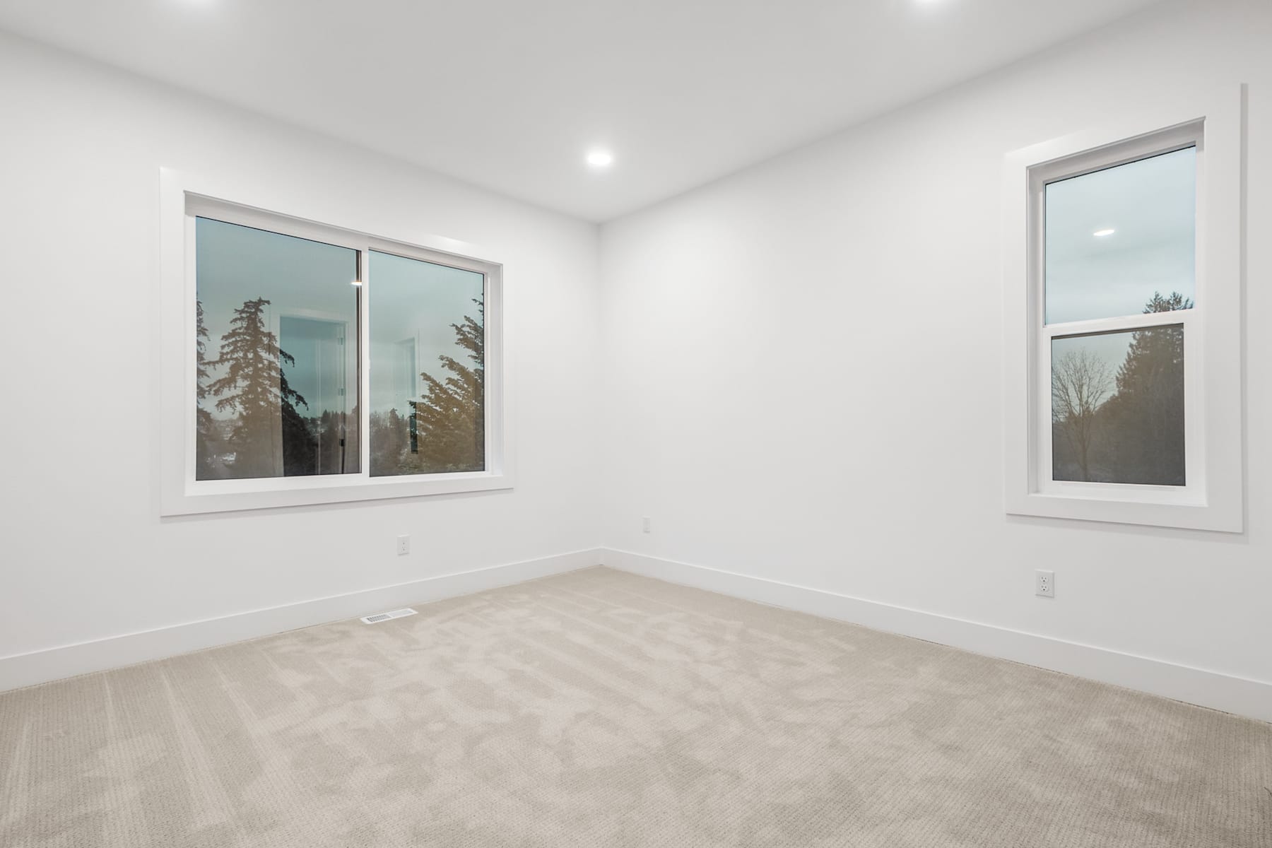 A bright, minimalist room with large windows overlooking a snowy forest landscape.