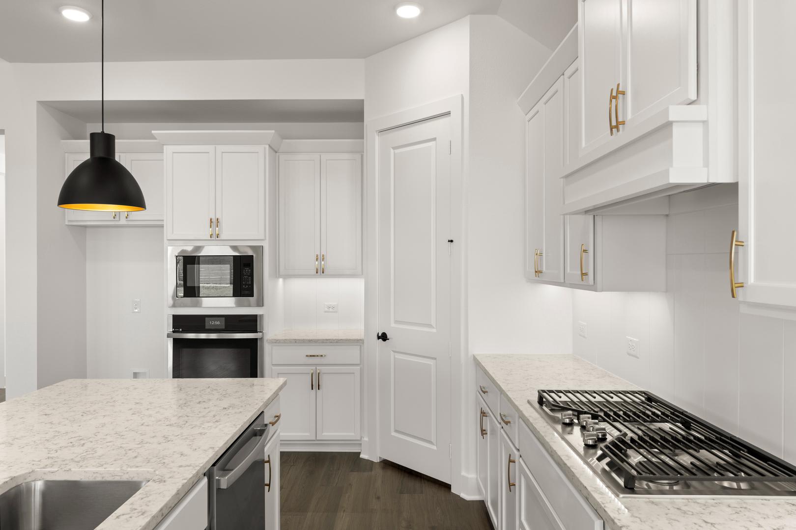 A modern, white kitchen with sleek cabinets, a marble countertop, and a black pendant light fixture.