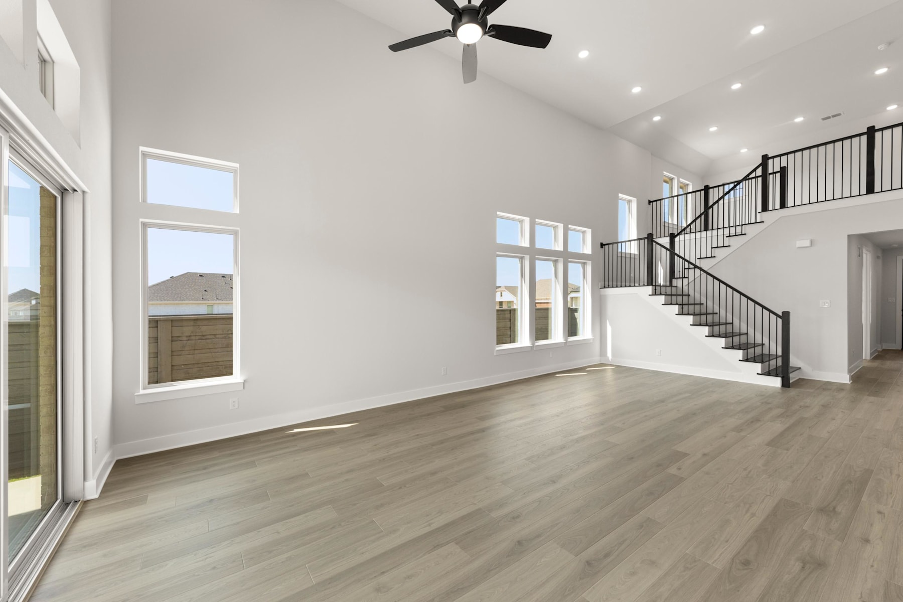A spacious and bright living room with hardwood floors, a ceiling fan, and a staircase leading to an upper level.