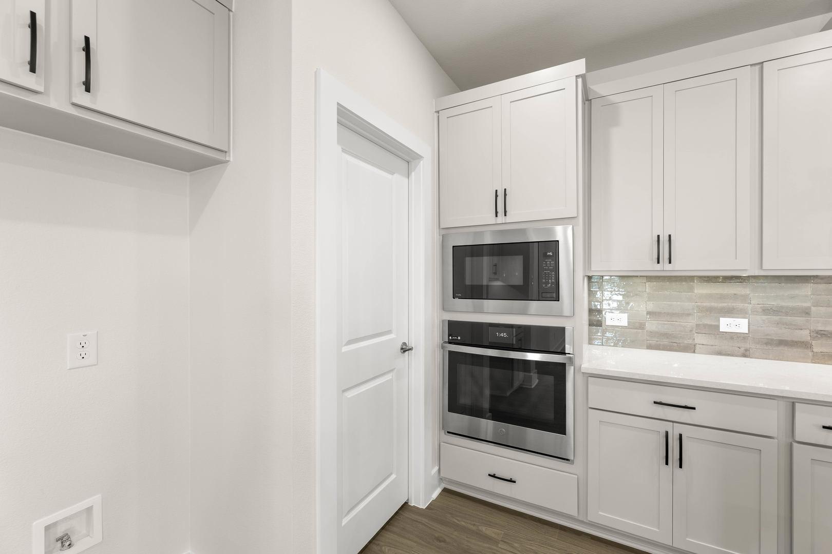 A modern, minimalist kitchen with white cabinets, stainless steel appliances, and a tiled backsplash.