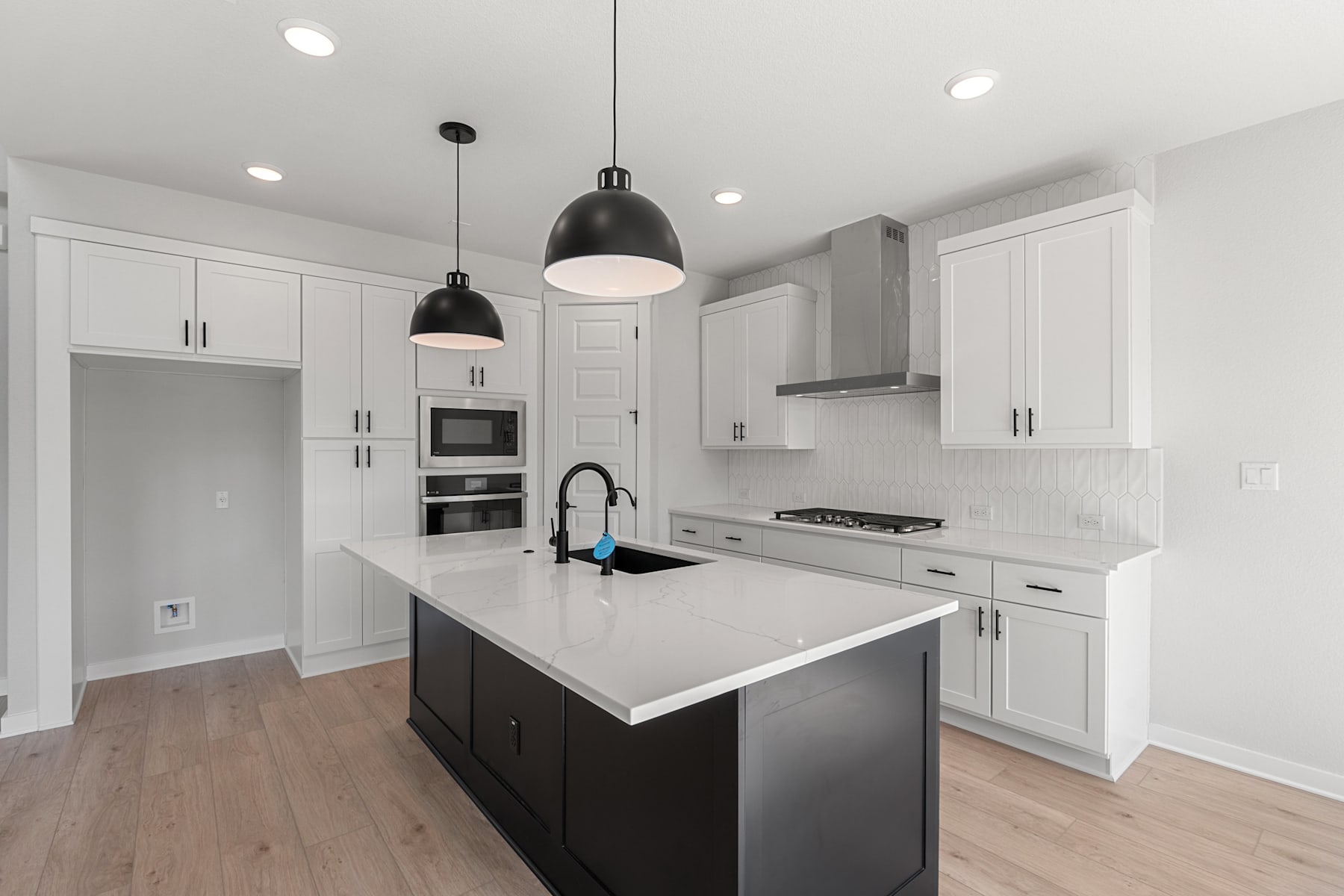 A modern, well-lit kitchen with white cabinets, a black island, and pendant lights hanging above the counter.