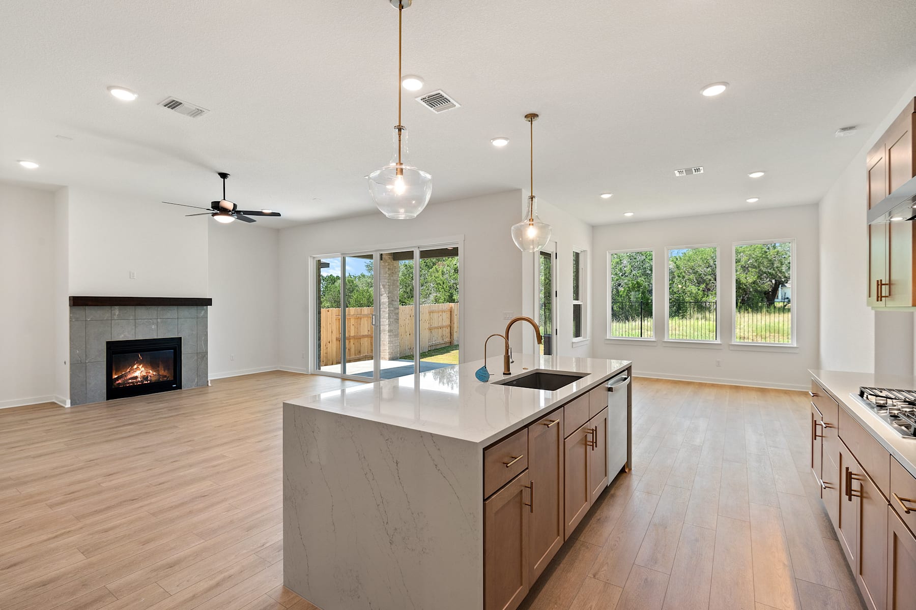 A modern, open-concept kitchen with a central island, hardwood floors, and large windows overlooking a backyard.