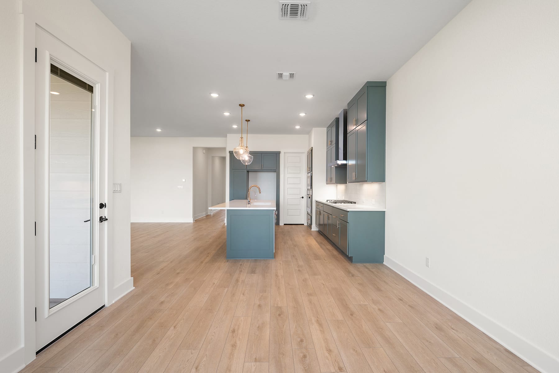 A modern, open-concept kitchen and living space with light-colored wood flooring, white walls, and teal-colored cabinets.