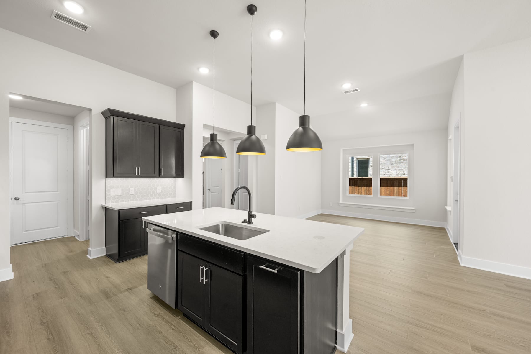 A modern, minimalist kitchen with sleek black cabinets, a white countertop, and pendant lights hanging above the island.