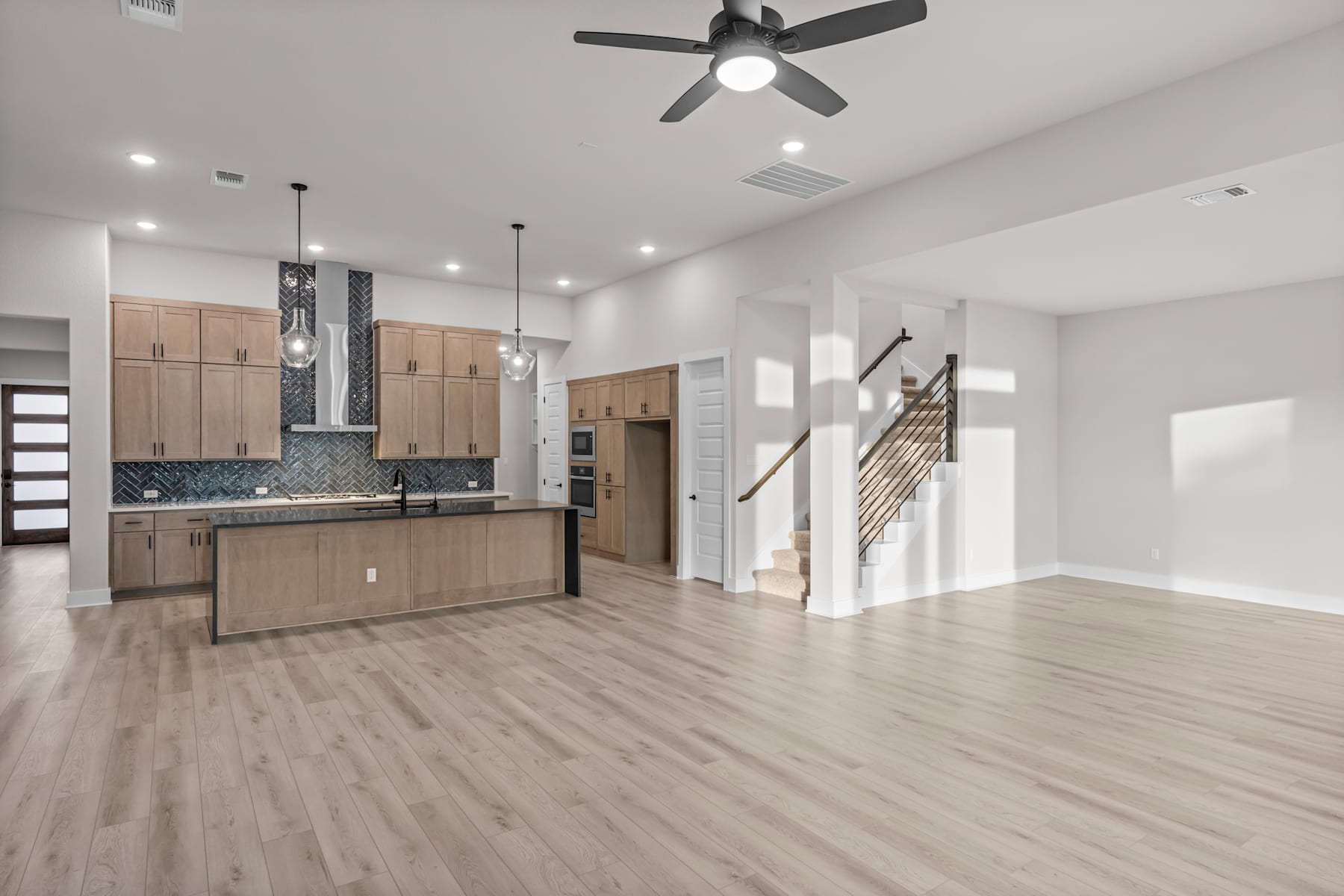 A modern, open-concept kitchen and living space with light-colored wood floors, neutral-toned cabinetry, and a ceiling fan.