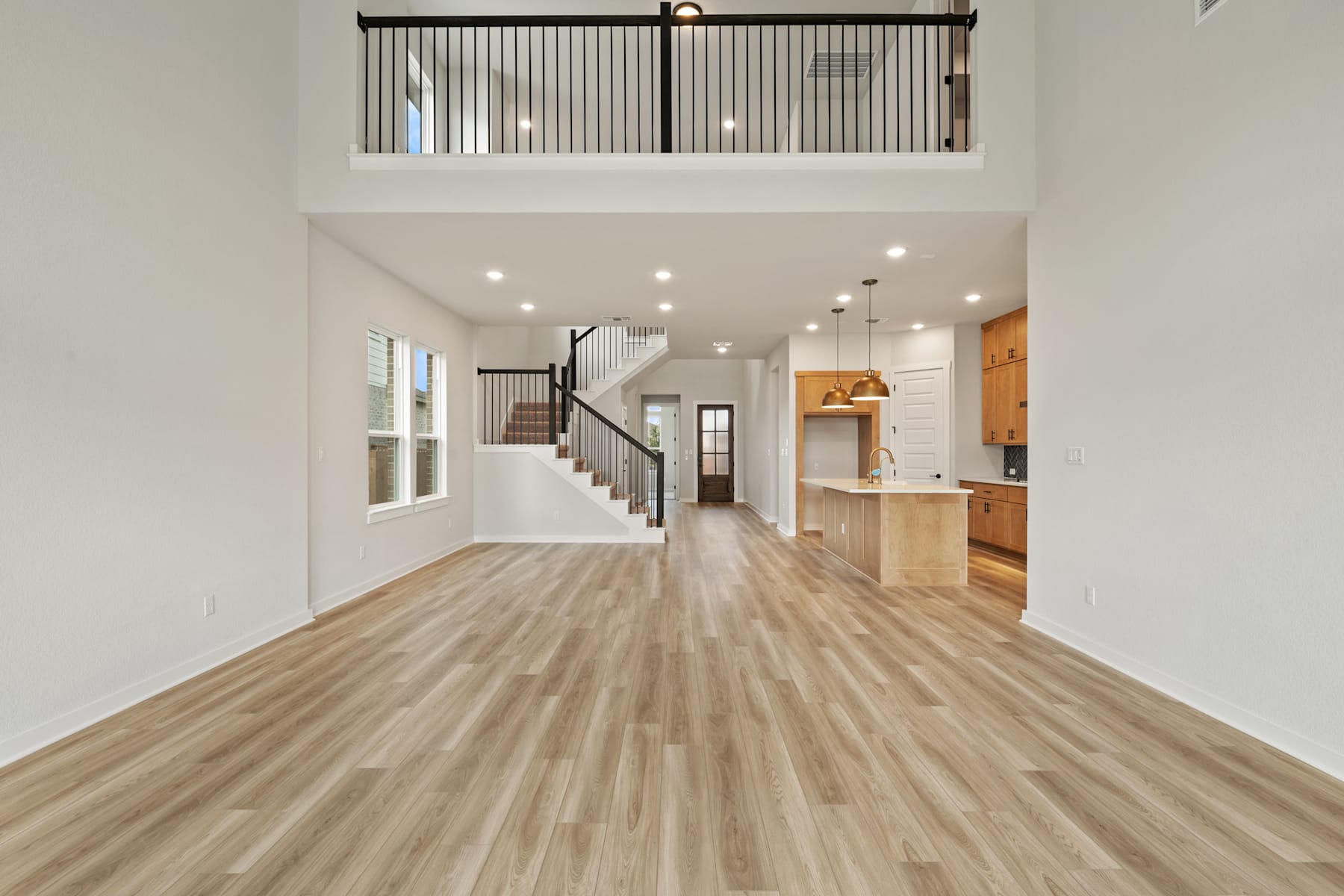 A spacious and modern interior with a wooden floor, a staircase, and a kitchen visible in the background.