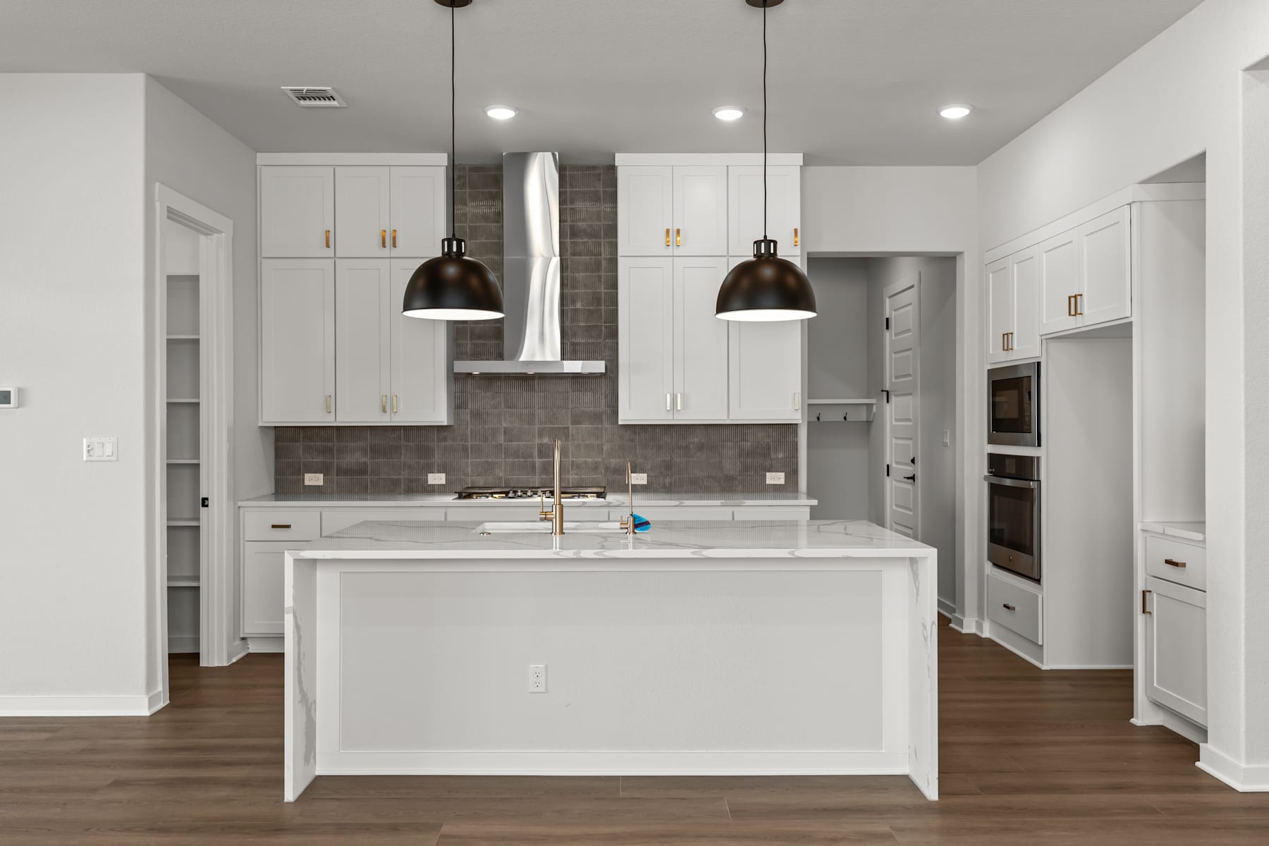 A modern, well-lit kitchen with white cabinets, a central island, and pendant lighting fixtures hanging above.