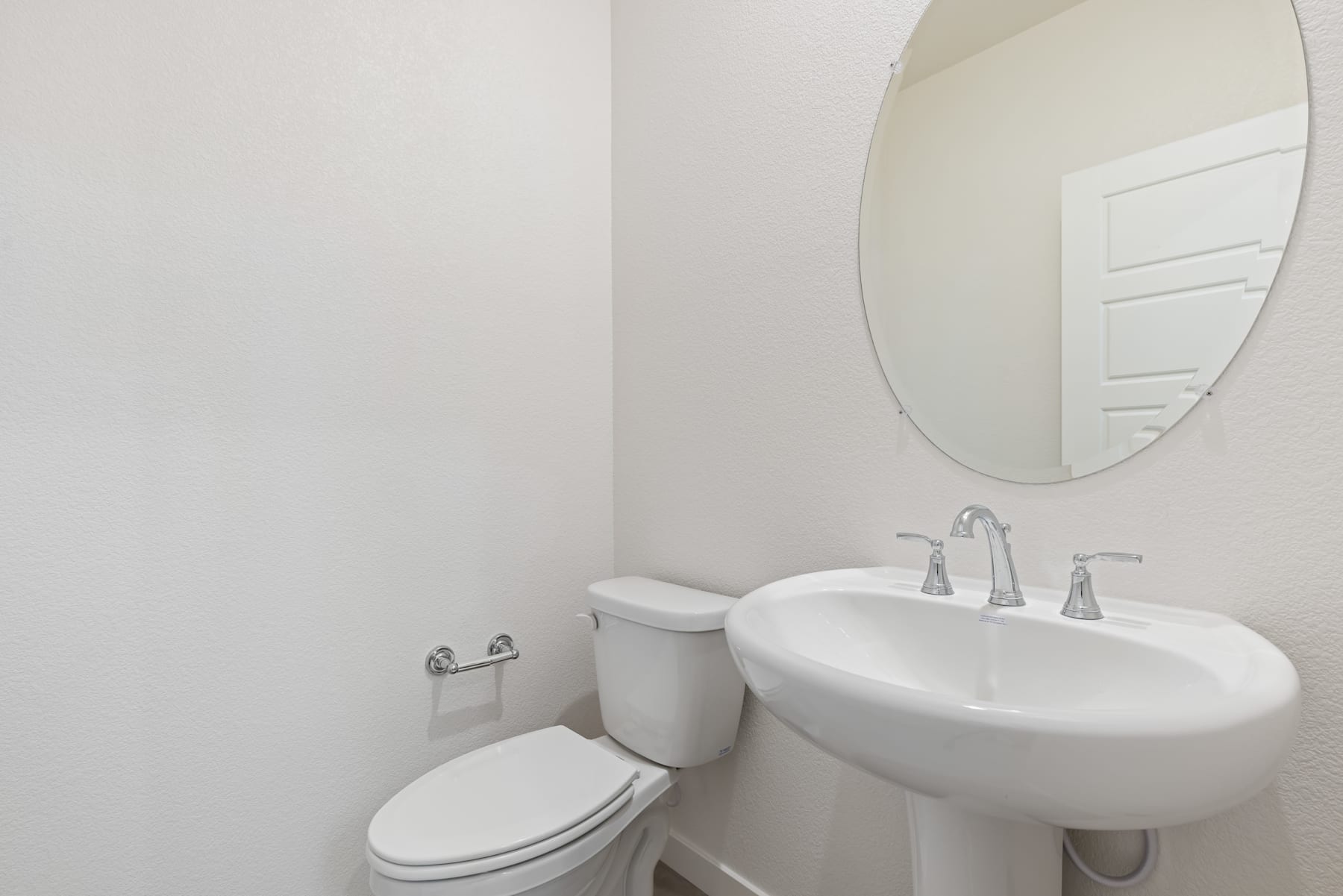 A simple and clean bathroom with a white toilet, sink, and a round mirror on the wall.