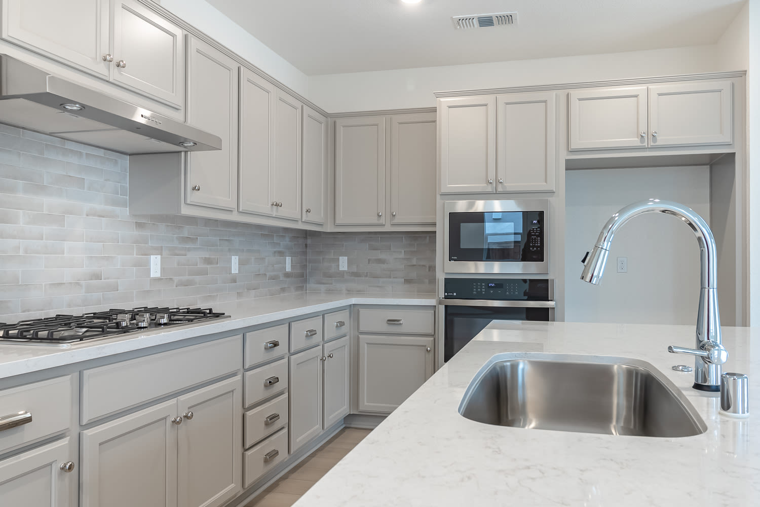 A modern, well-equipped kitchen with white cabinets, a stainless steel sink, and a tiled backsplash.