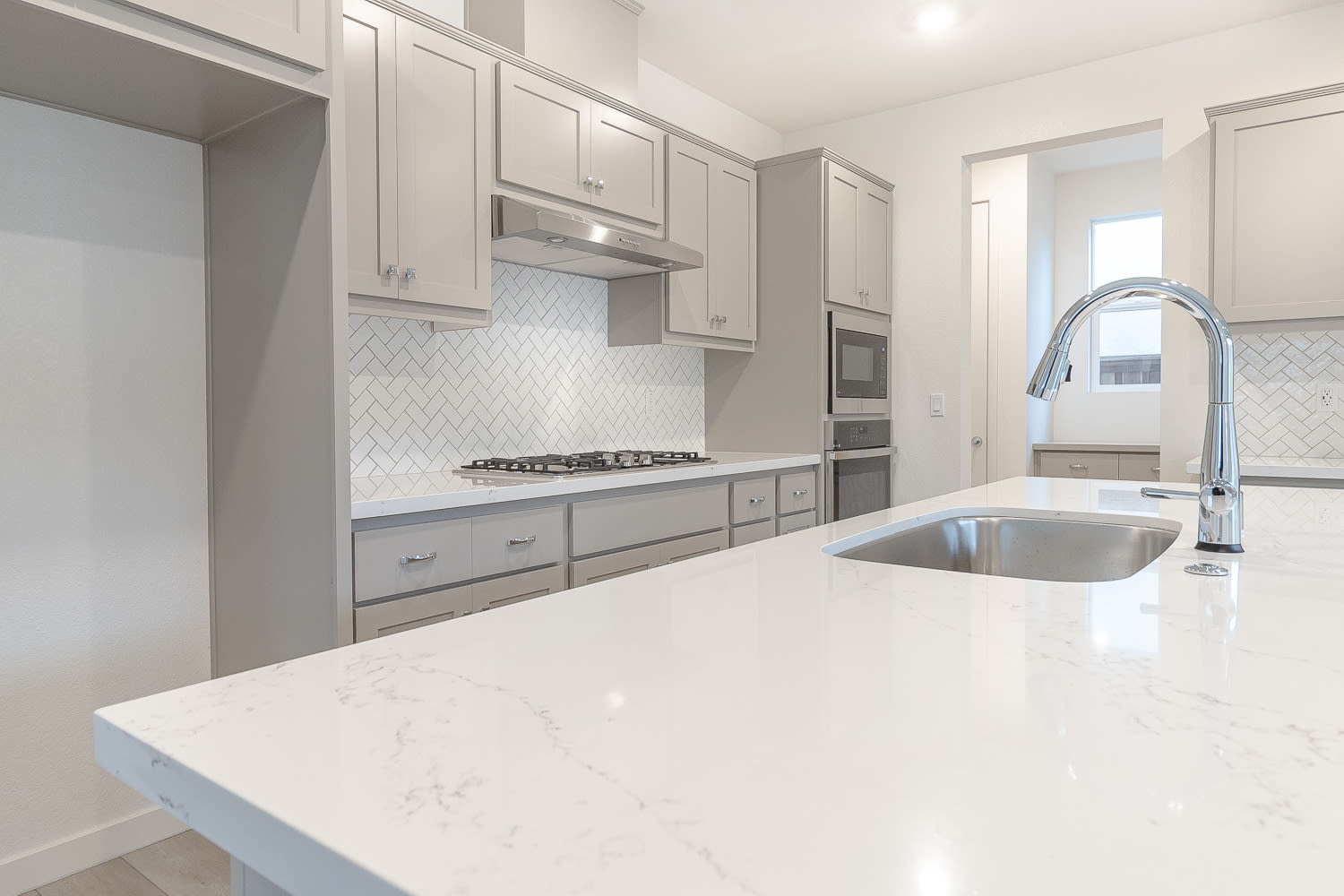 A modern, well-equipped kitchen with white cabinets, a marble-like countertop, and a stainless steel sink and faucet.