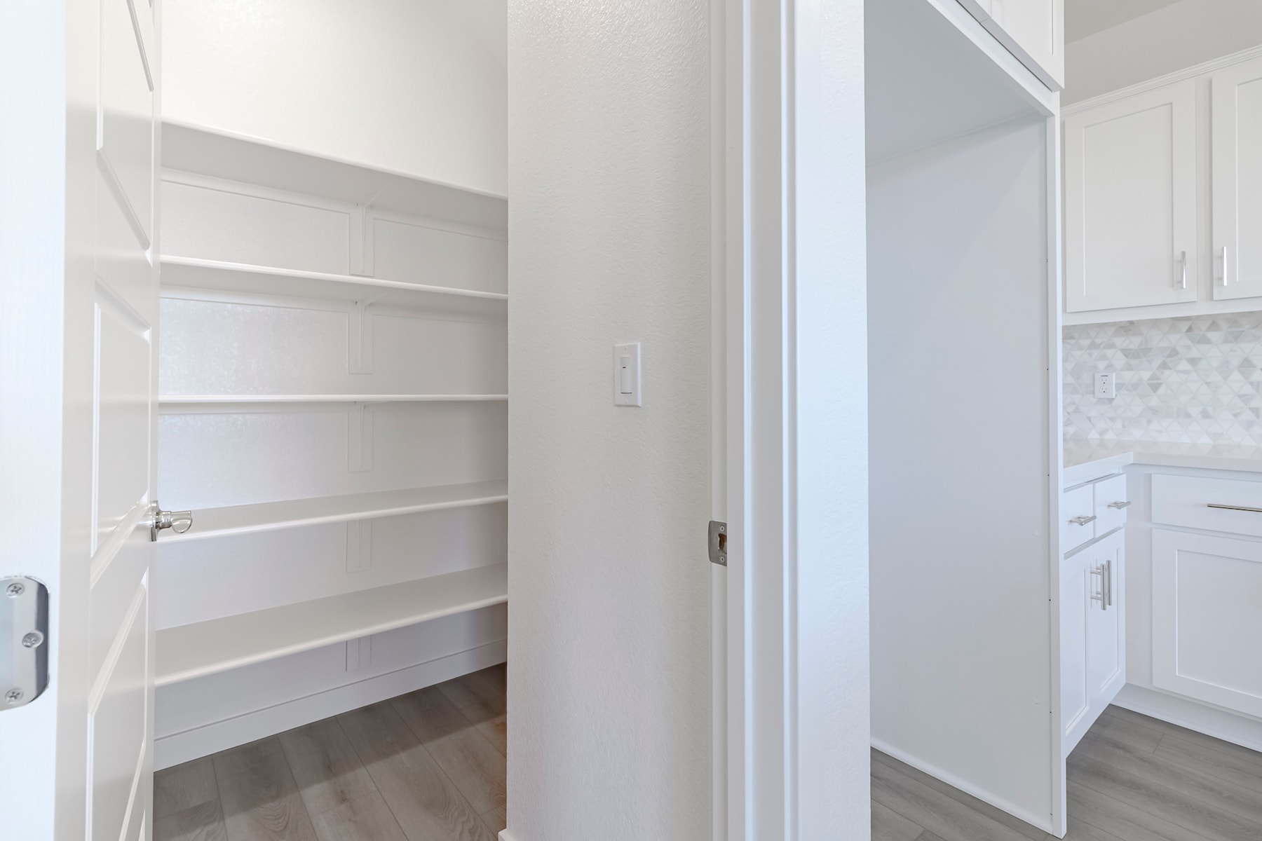 A white, minimalist interior with open shelving and a partially visible doorway leading to another room.