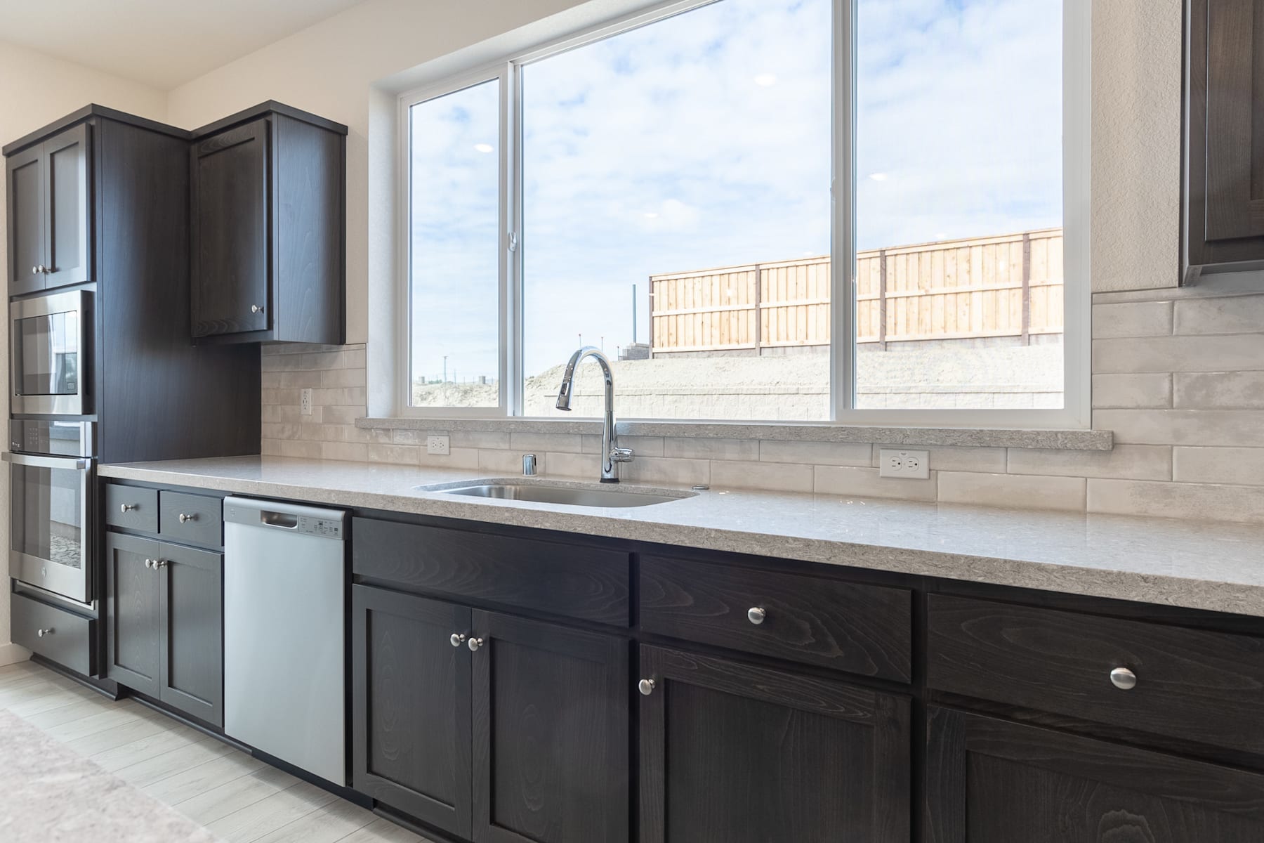 A modern kitchen with dark cabinets, a large window, and a tiled backsplash.