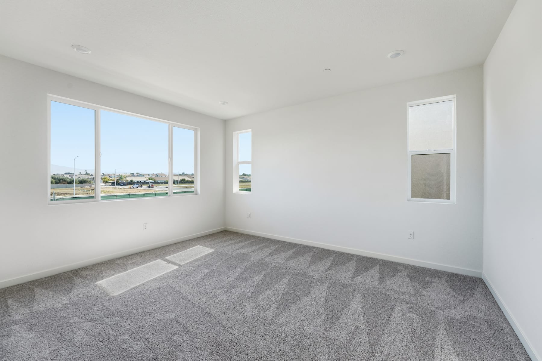 A spacious, well-lit room with large windows overlooking a scenic outdoor landscape, featuring a gray patterned floor and a minimalist design aesthetic.