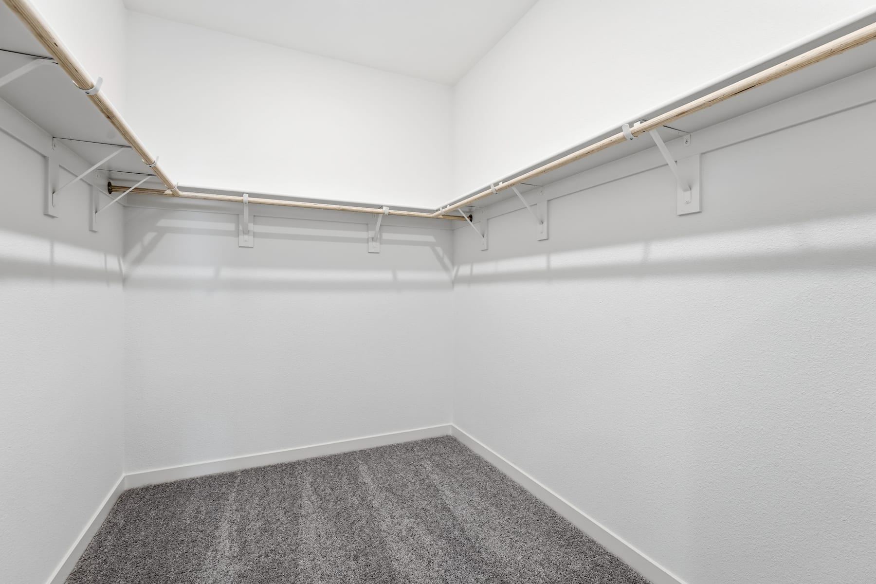 A white, empty closet with a gray carpeted floor and metal clothing rods along the walls.
