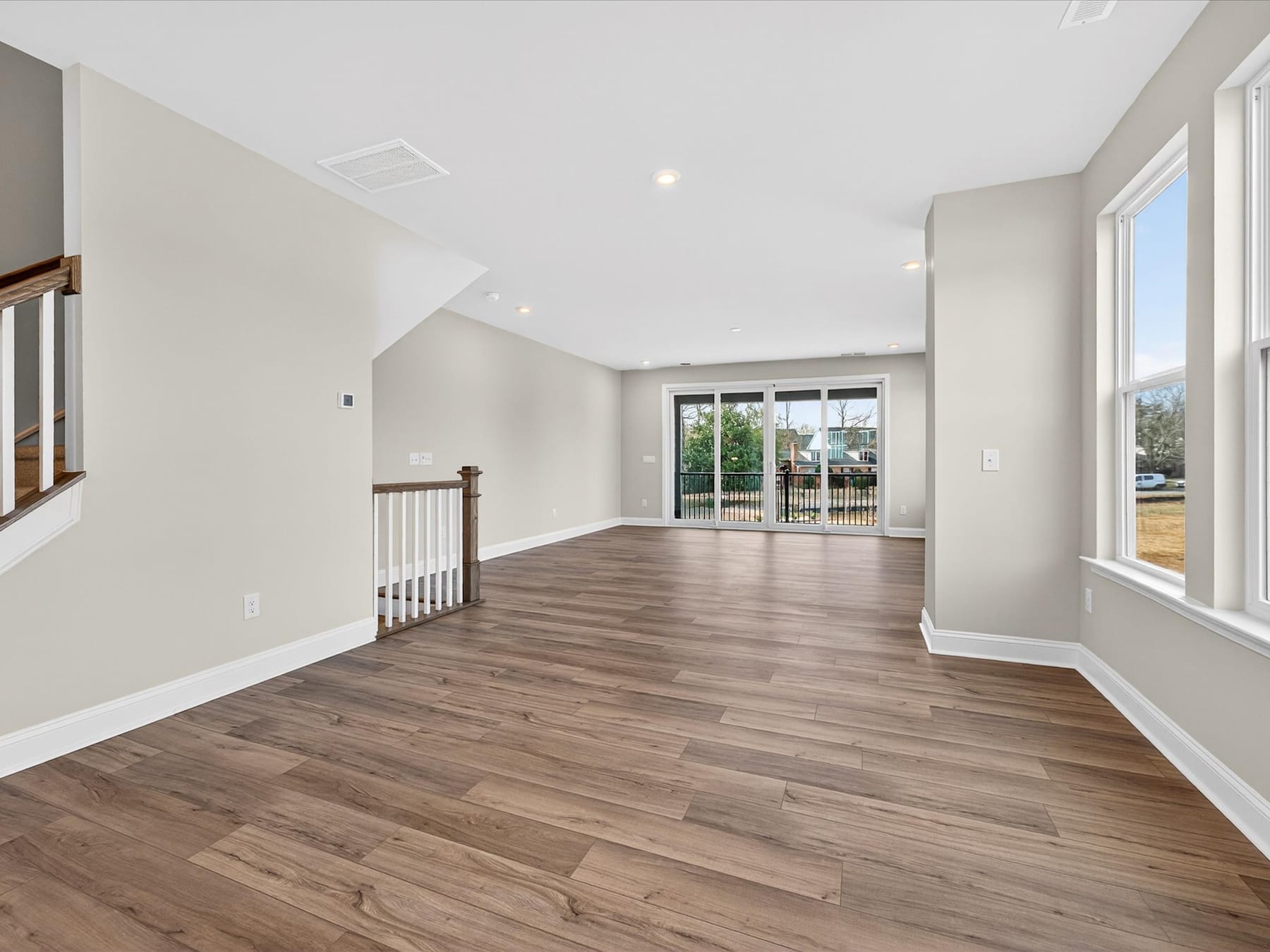 A spacious, open-concept room with hardwood floors, white walls, and a large window overlooking an outdoor area.