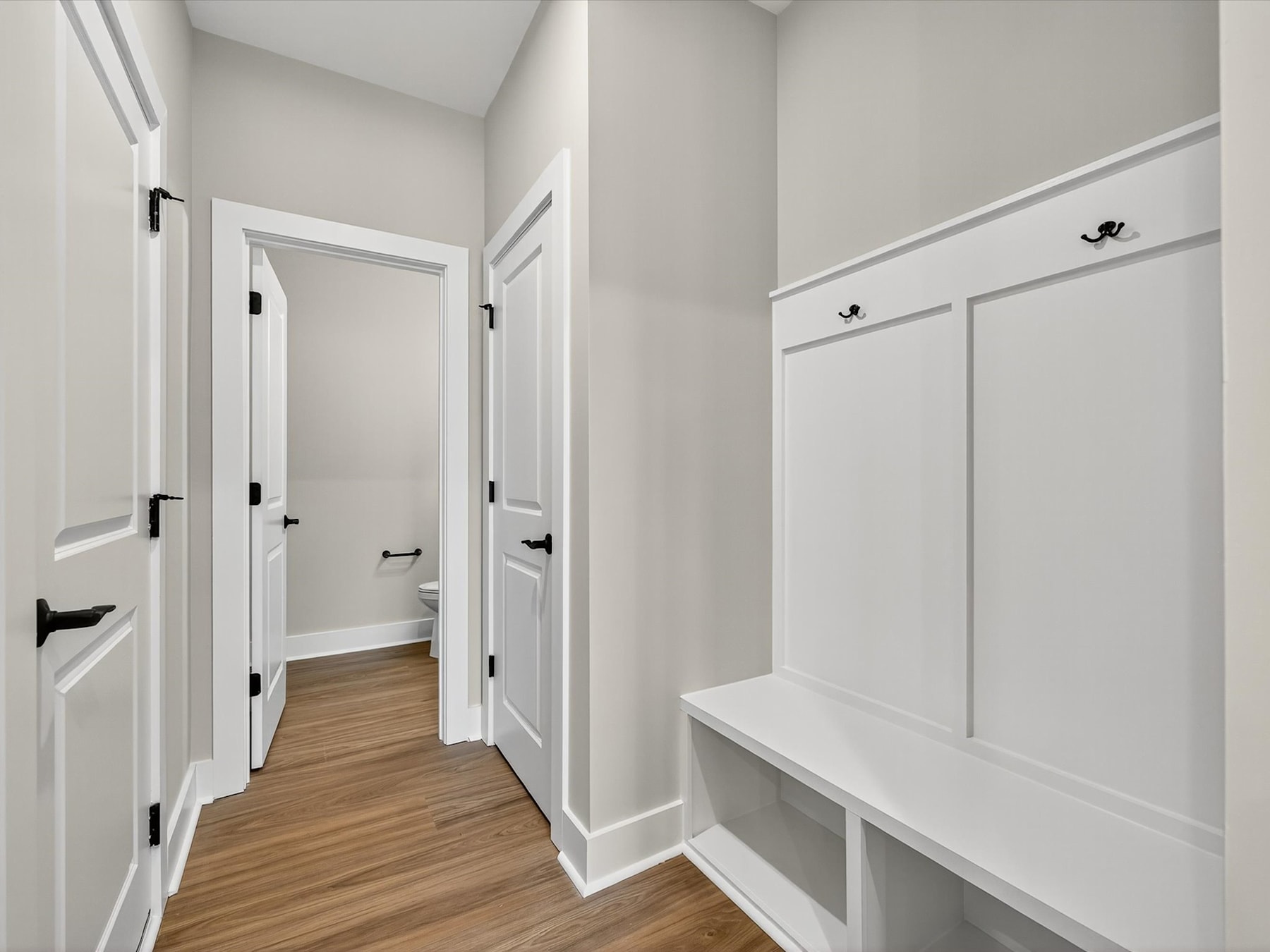 A bright, minimalist hallway with white walls, wooden floors, and built-in storage cabinets along the walls.