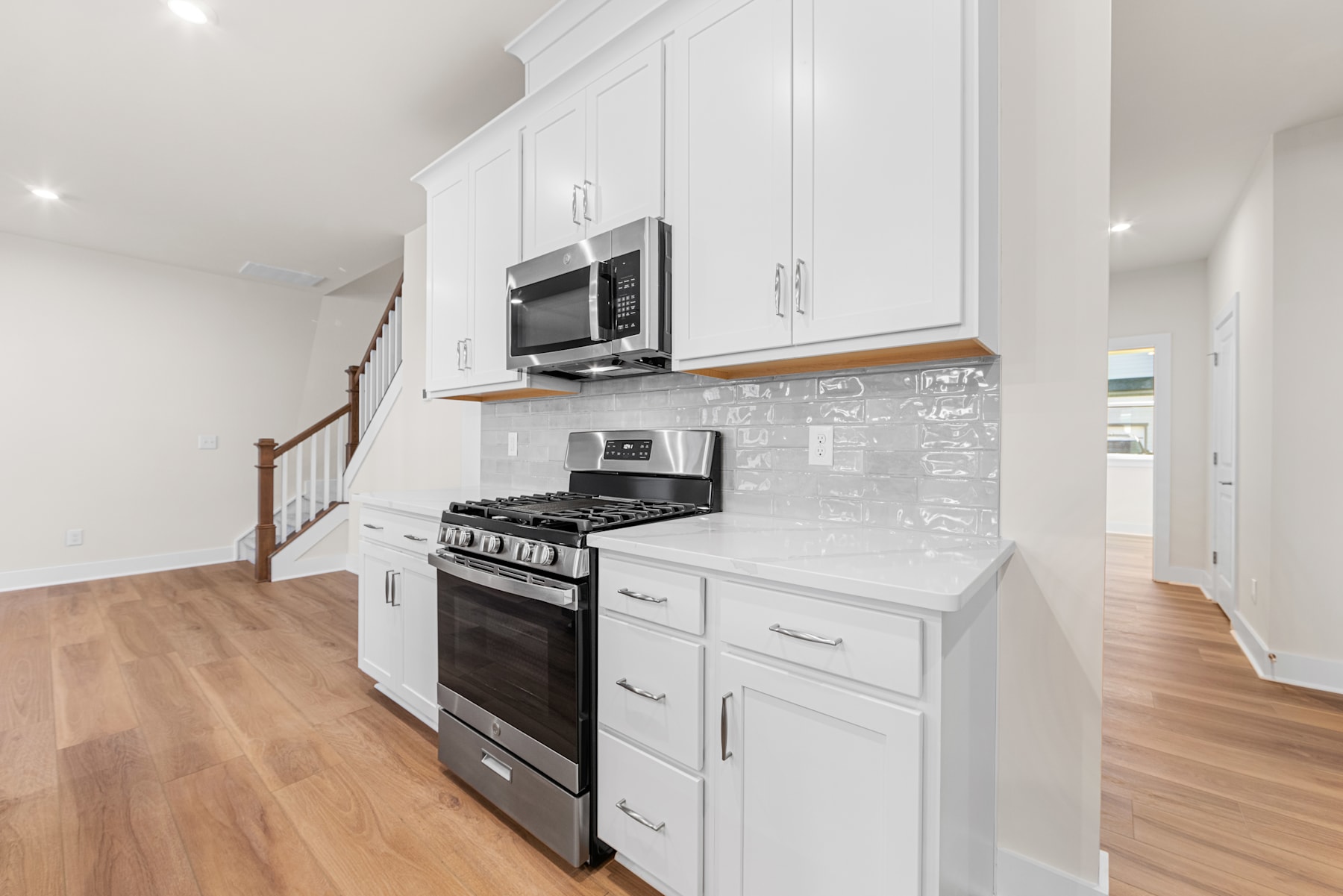 A modern, well-equipped kitchen with white cabinets, a stainless steel oven, and a hardwood floor, set against a bright and airy background.
