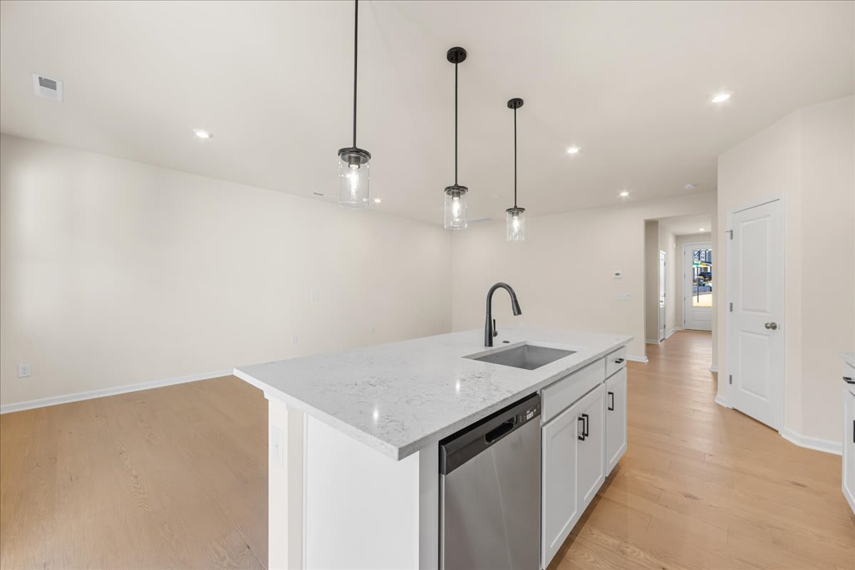 A modern, minimalist kitchen with white countertops, stainless steel appliances, and pendant lighting fixtures hanging from the ceiling.