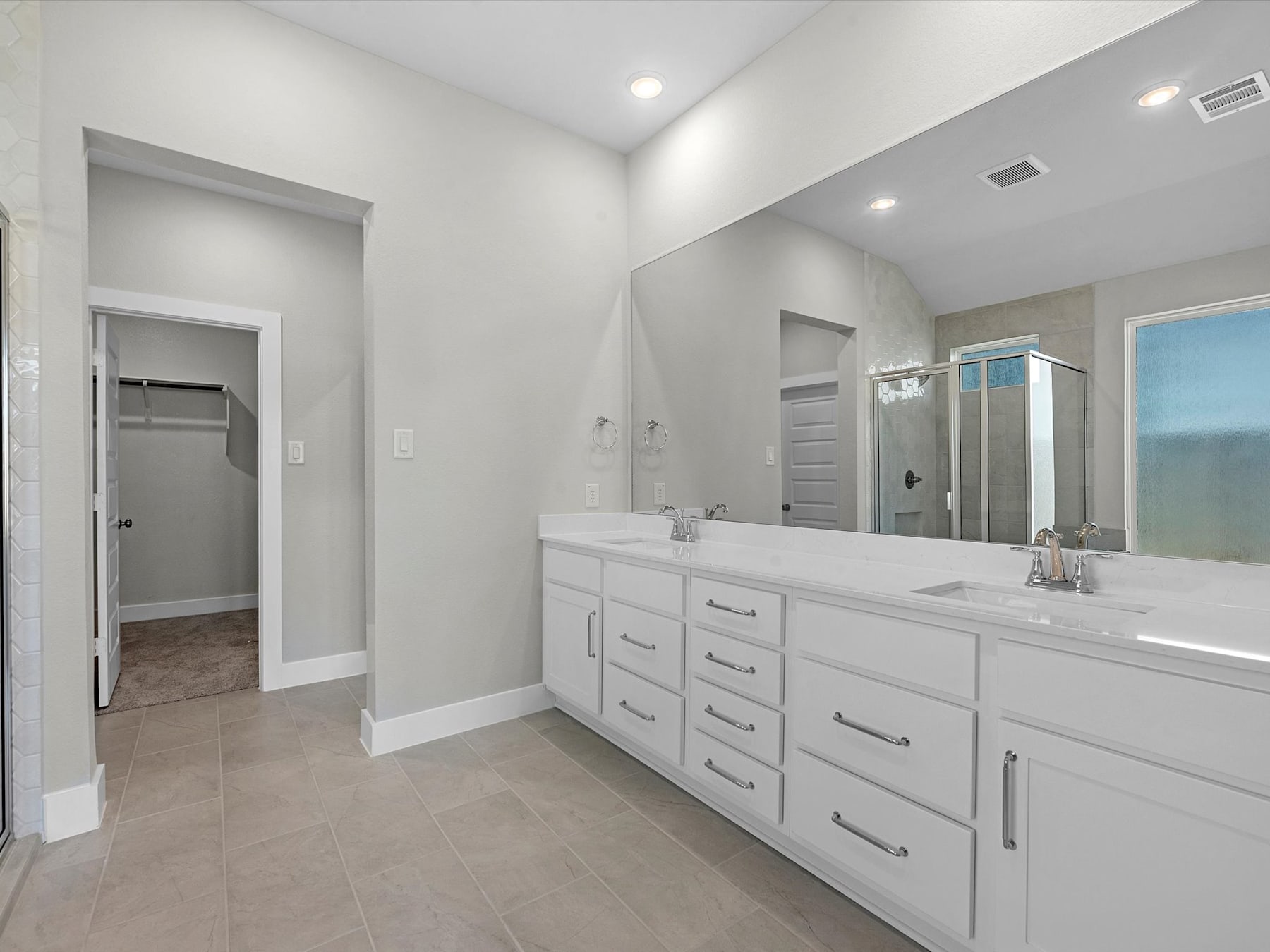 A spacious and modern bathroom with a large vanity, white cabinets, and a tiled floor.