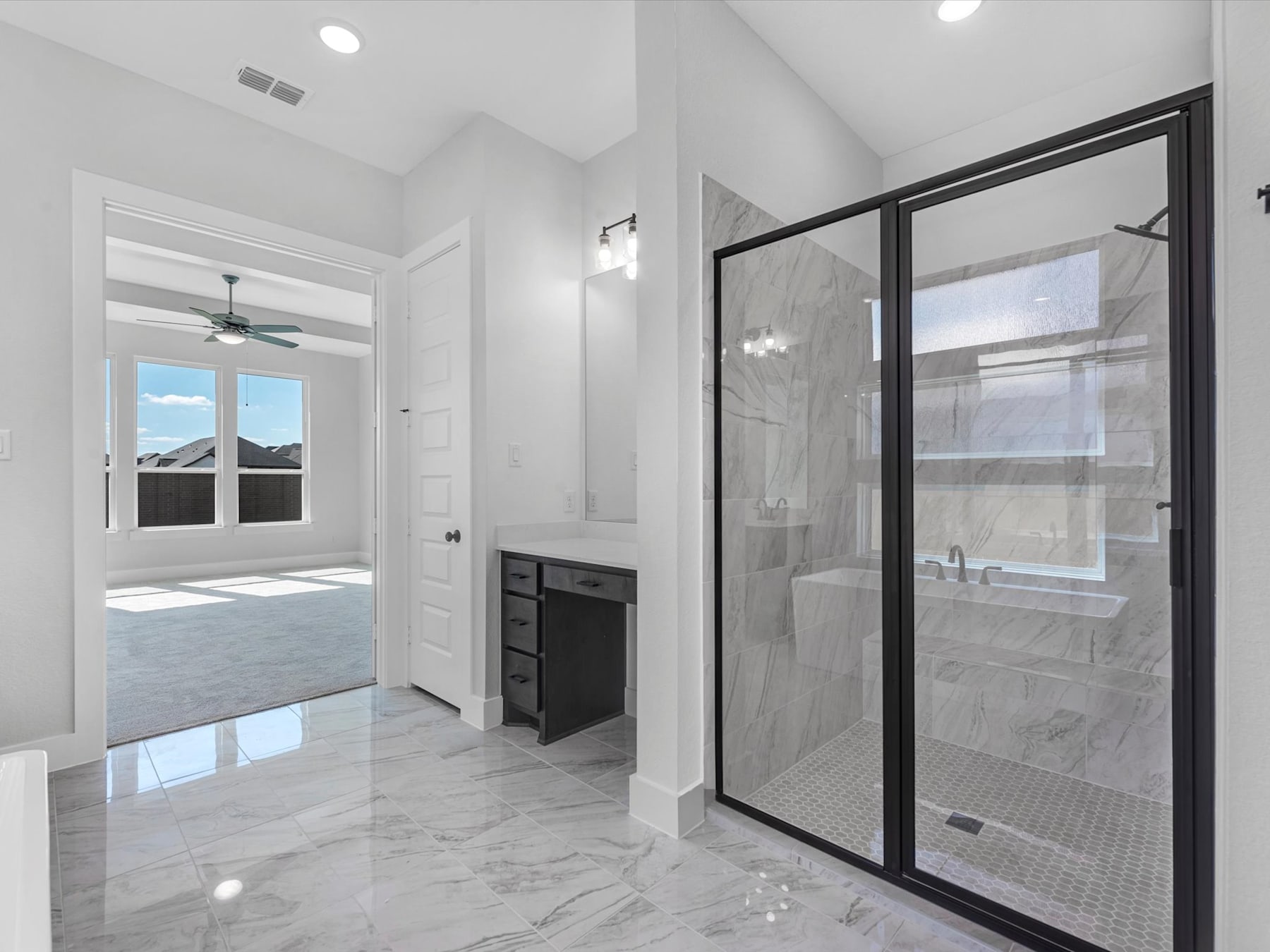 A spacious and modern bathroom with a large glass-enclosed shower, sleek black fixtures, and a marble-tiled floor that reflects the natural light streaming in through the windows.