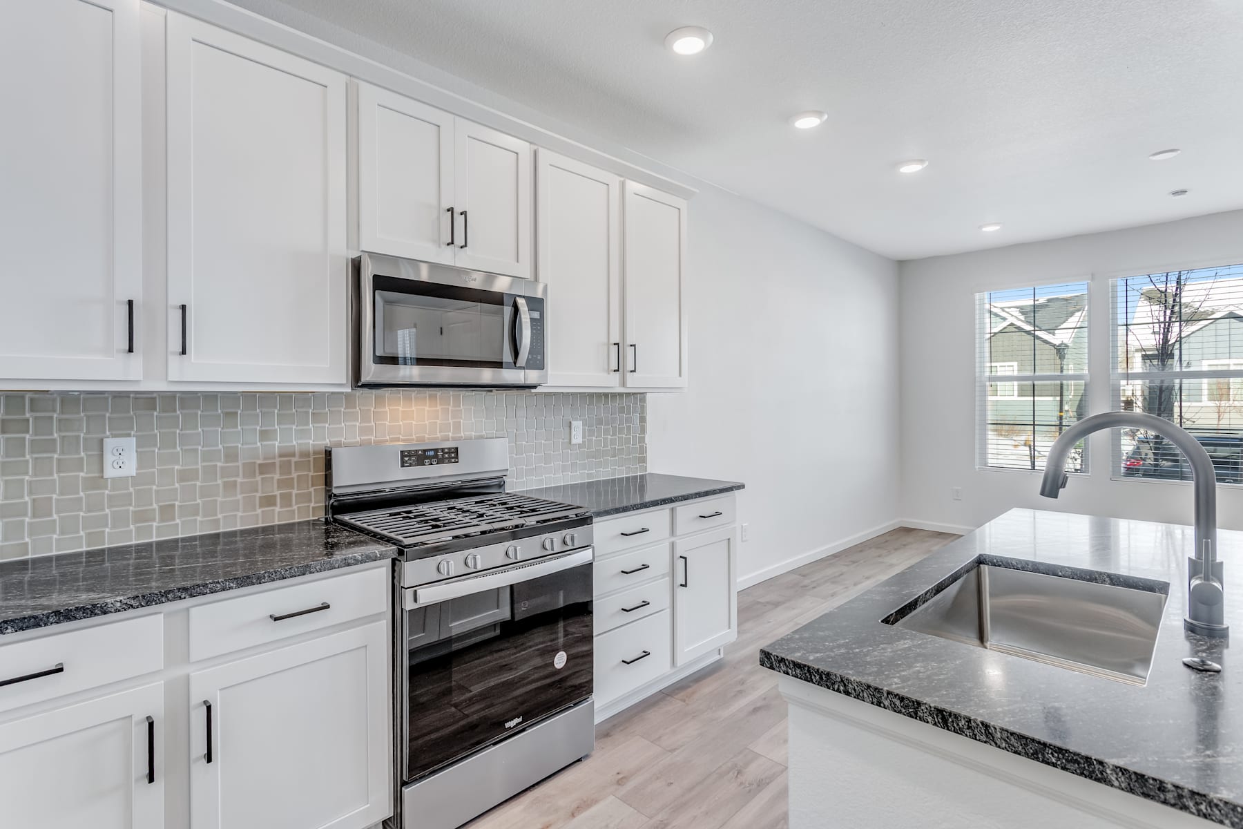 A modern, well-equipped kitchen with white cabinets, stainless steel appliances, and a tiled backsplash, set against a bright and airy background.