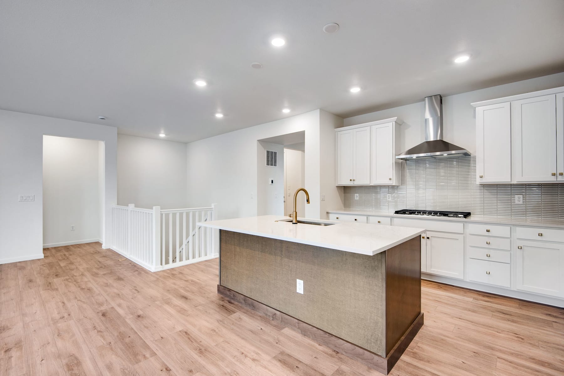 A modern, open-concept kitchen with white cabinets, a central island, and hardwood flooring, set against a bright and airy background.