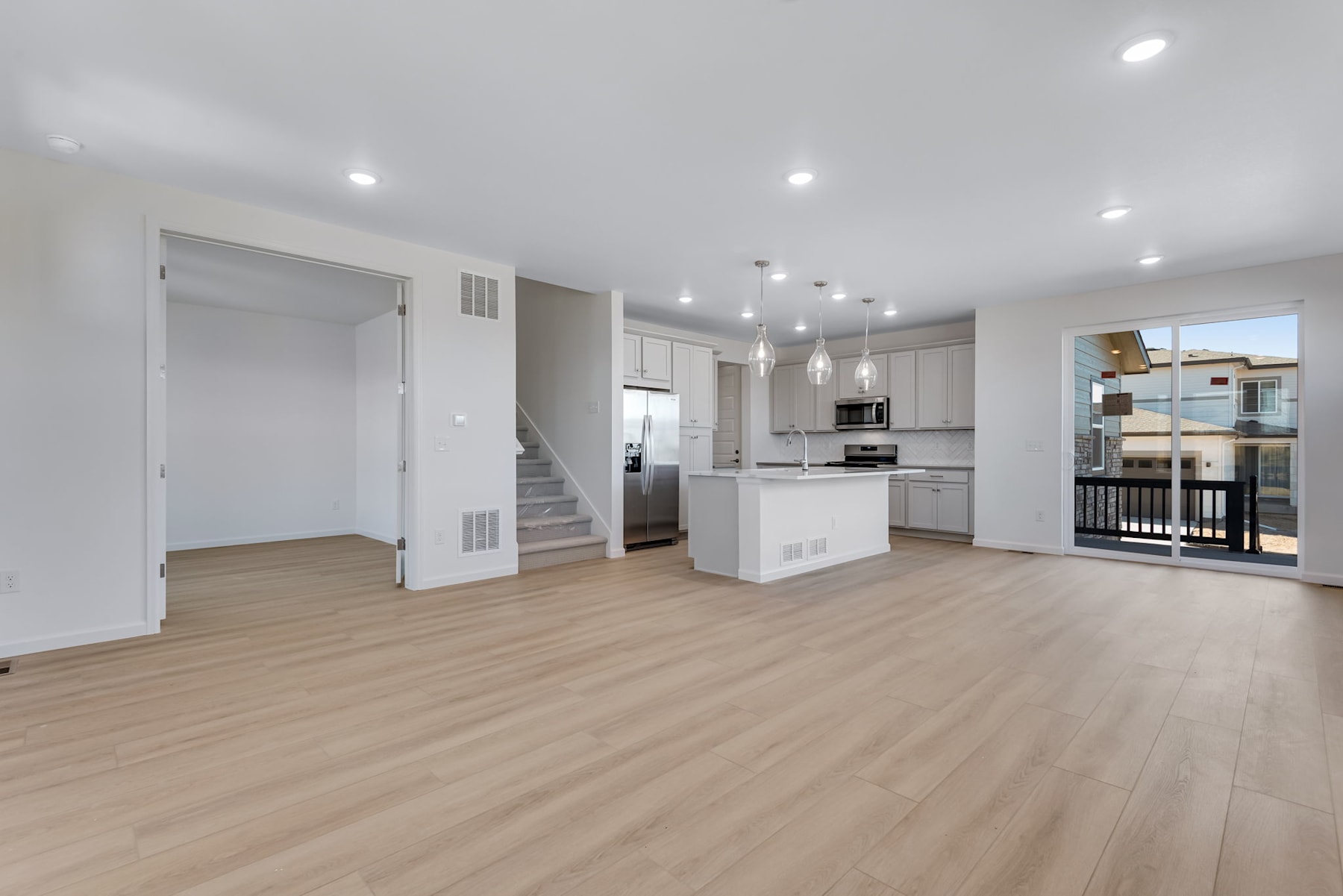 A bright and spacious open-concept kitchen and living room with white cabinets, hardwood floors, and a balcony visible in the background.
