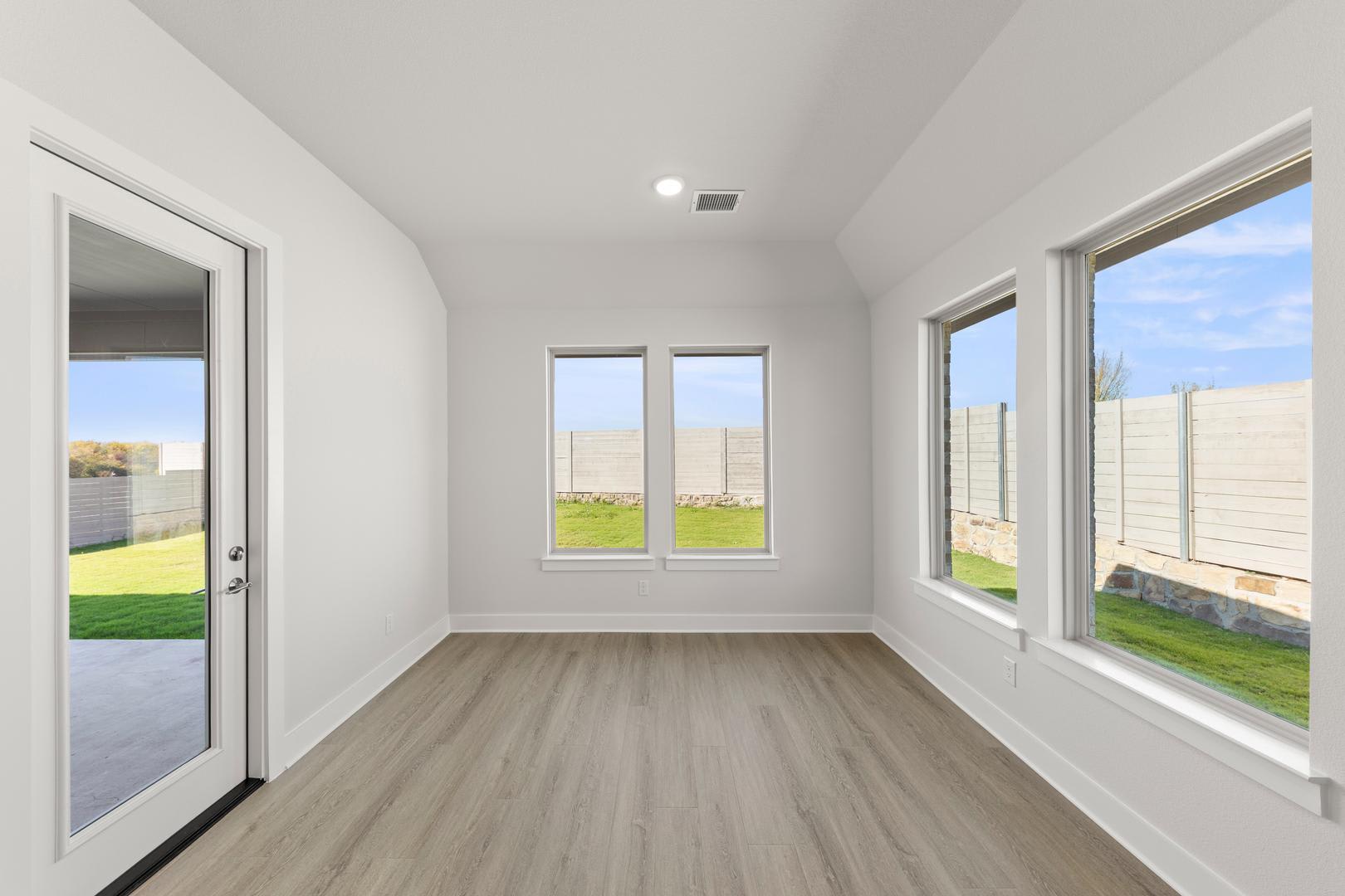A bright, spacious room with large windows overlooking a grassy outdoor area, featuring a hardwood floor and a white interior.