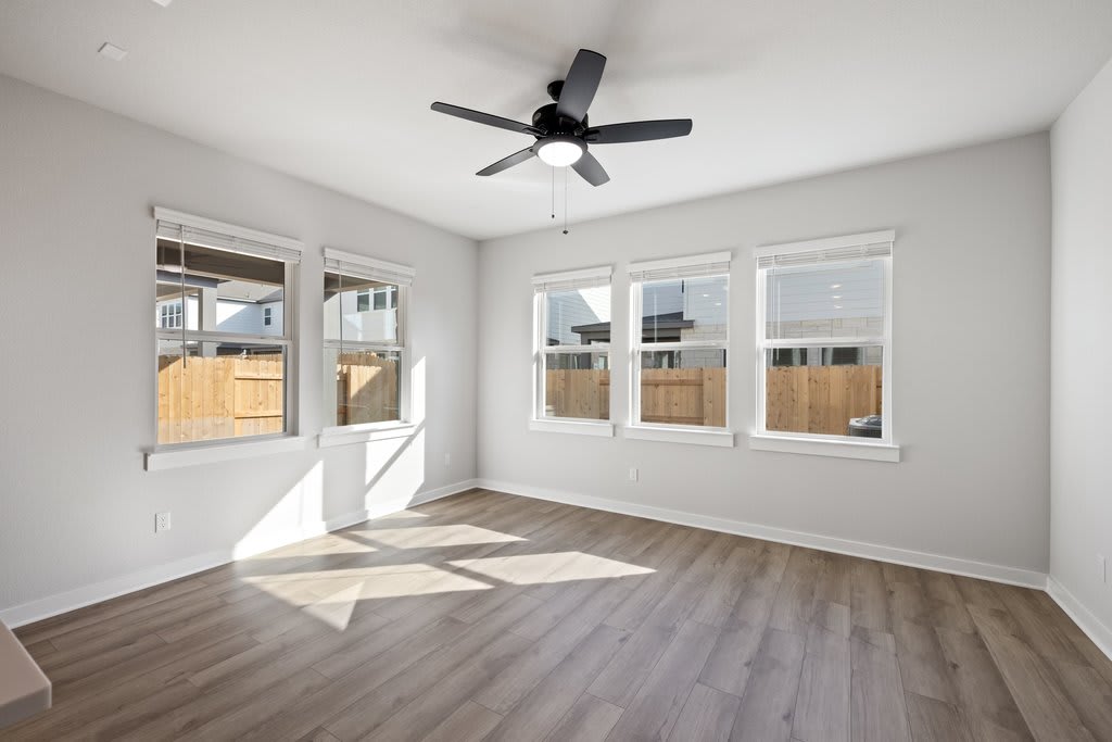 A bright and airy room with a ceiling fan, wooden floors, and large windows overlooking a backyard.