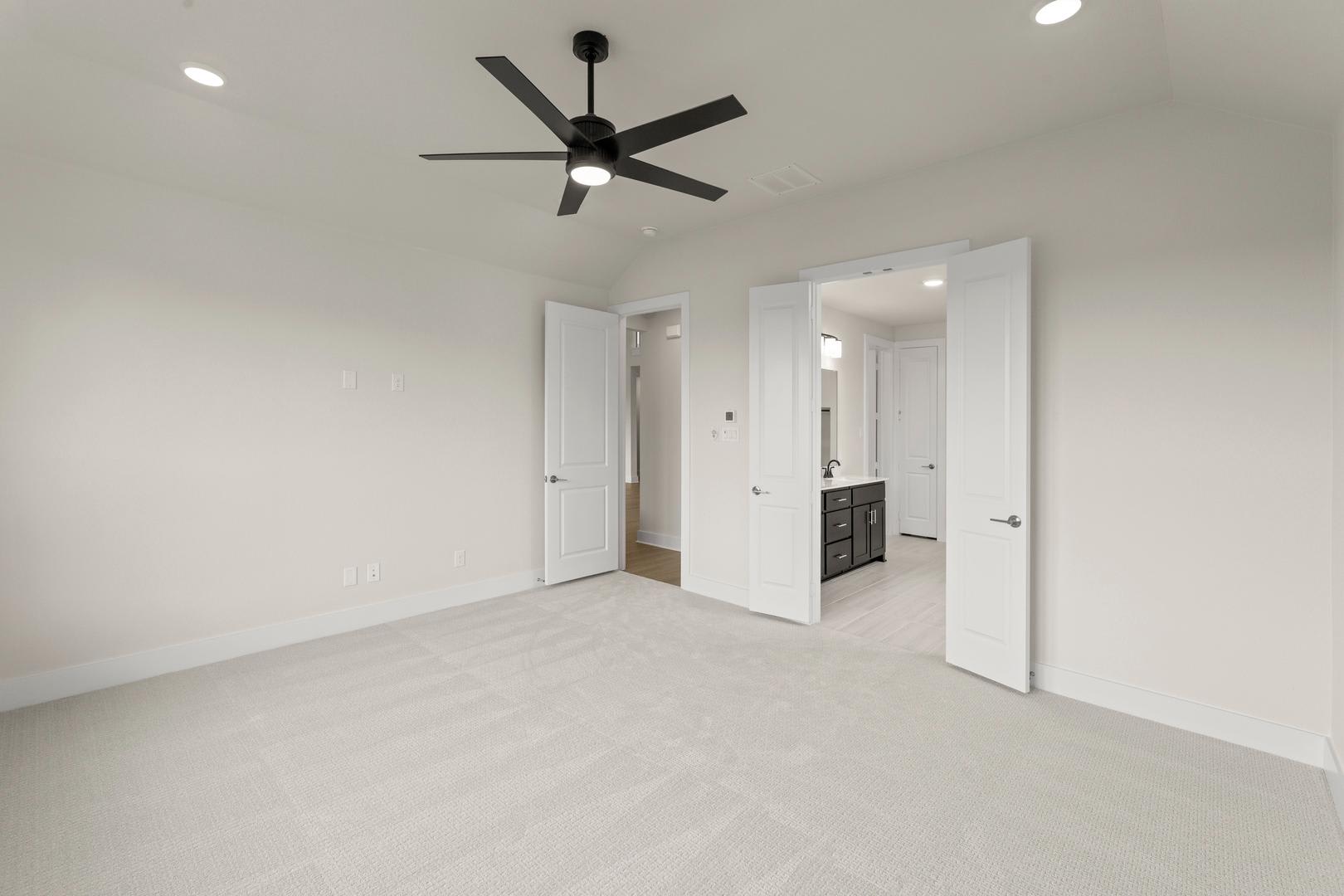 A spacious, minimalist room with a ceiling fan and white walls, featuring open doorways leading to other areas.