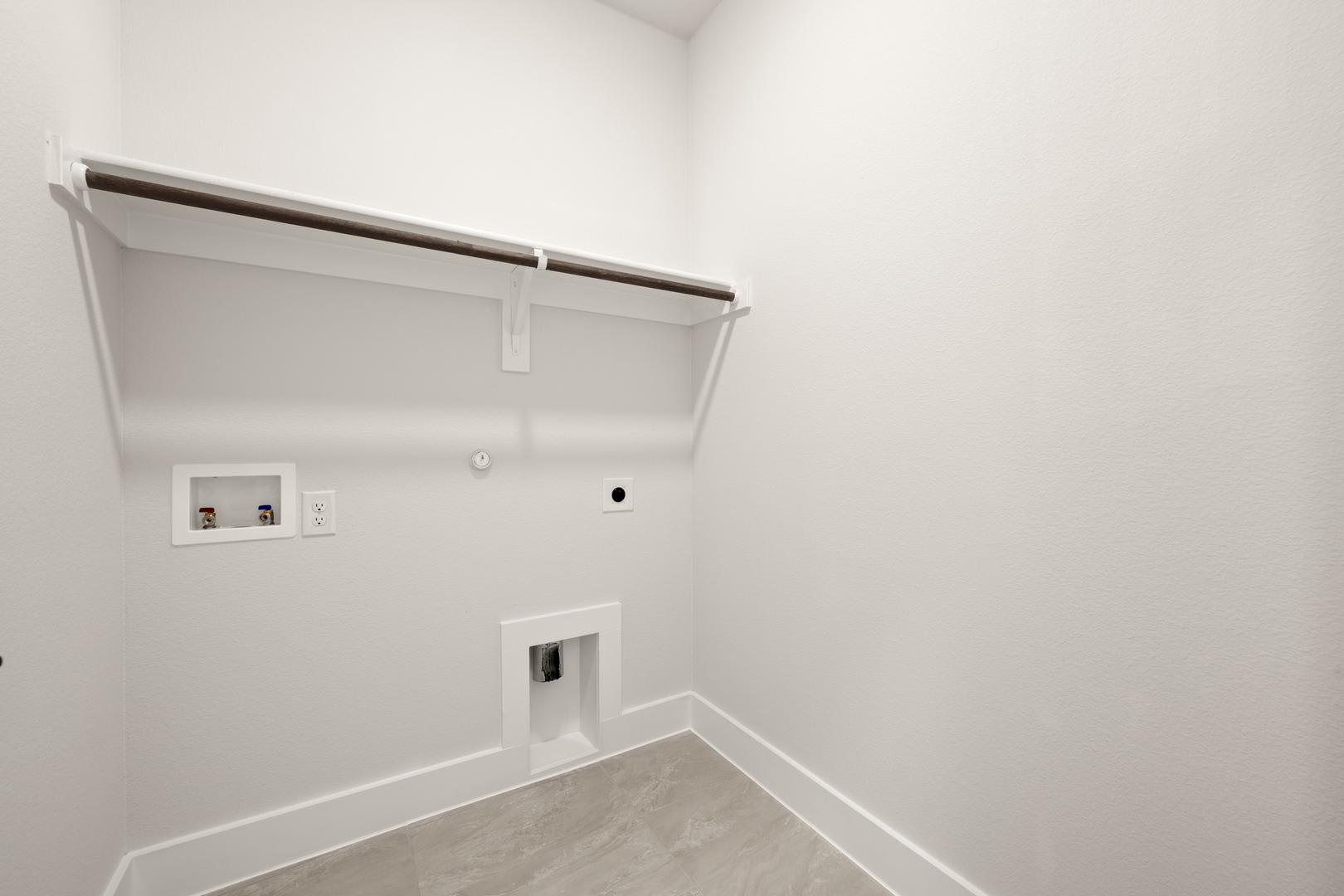 A simple, minimalist closet space with white walls, a hanging rod, and a power outlet visible in the corner.