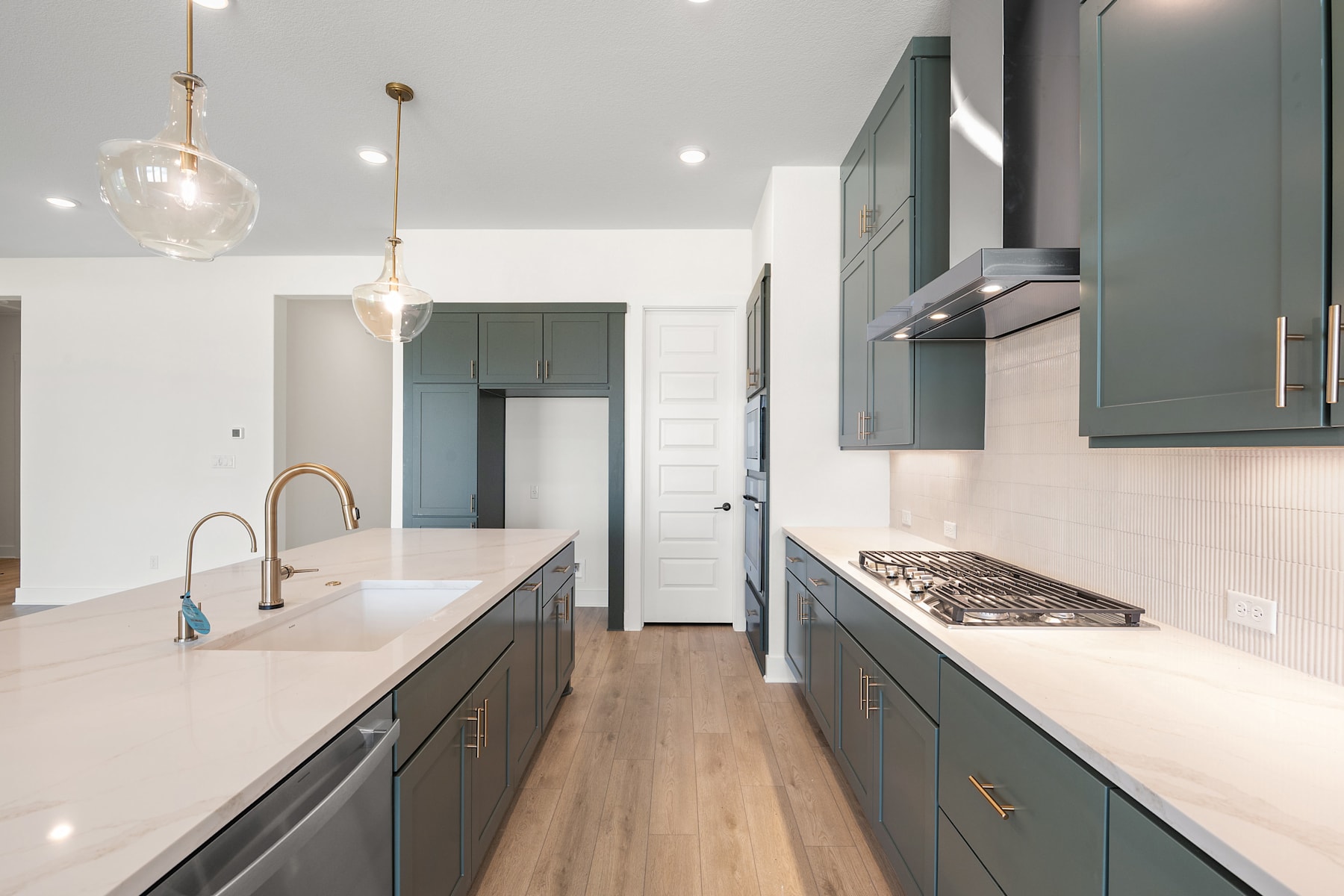 A modern, well-designed kitchen with gray cabinets, white countertops, and pendant lighting fixtures, leading into a hallway or other room.