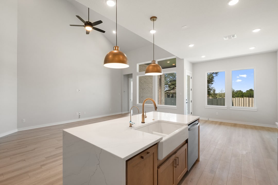 A modern kitchen with a white sink, copper pendant lights, and a ceiling fan, set against a backdrop of large windows overlooking a scenic outdoor view.