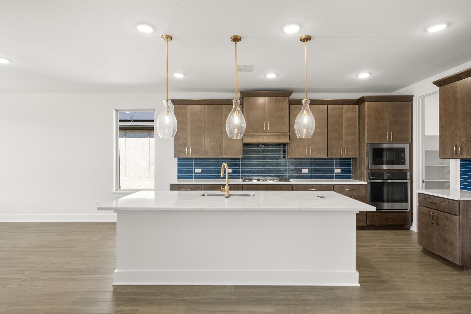 A modern and spacious kitchen with wooden cabinets, a white island, and pendant lights illuminating the space.