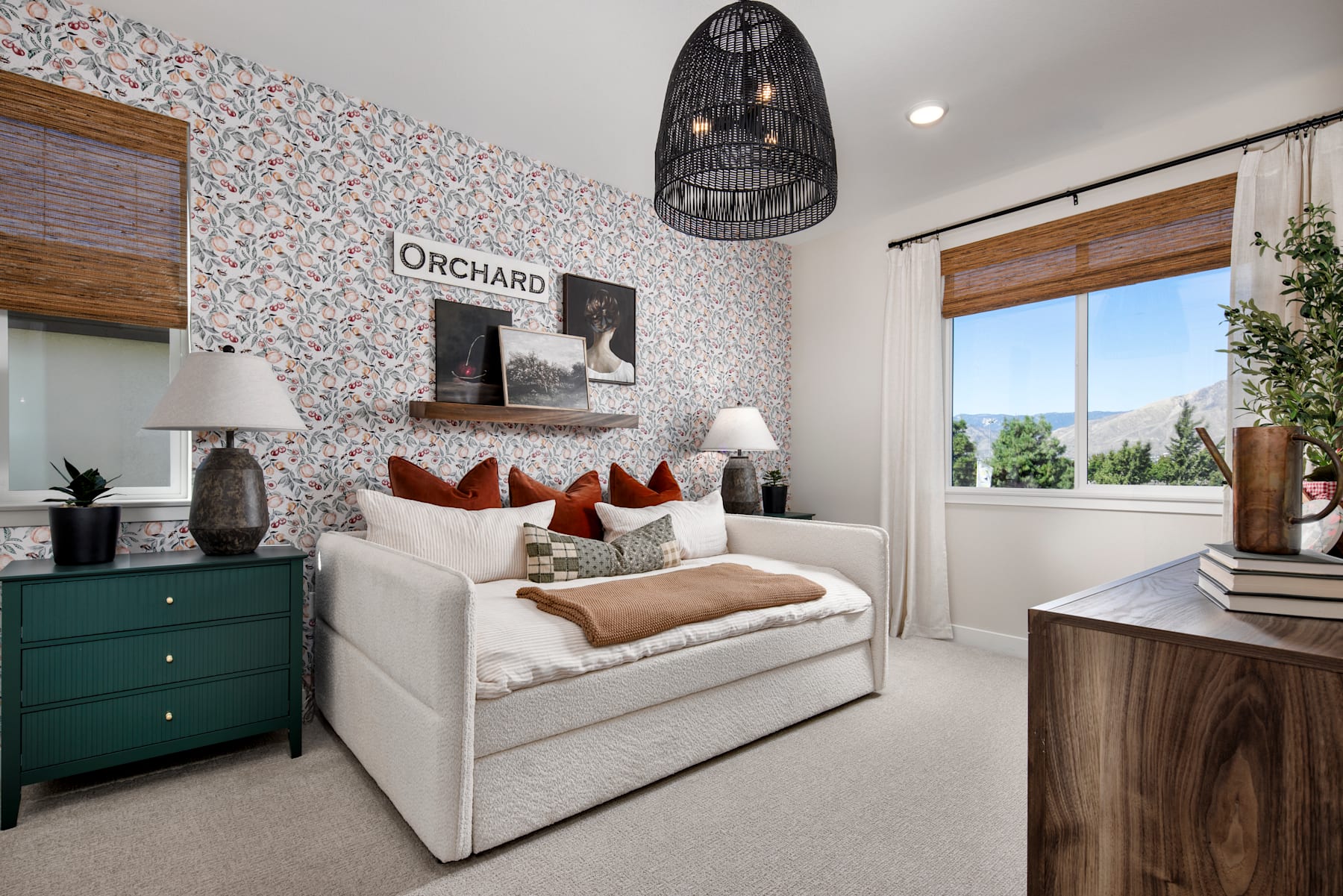 A cozy and inviting bedroom with a white sofa, a green dresser, and a large birdcage-shaped light fixture hanging from the ceiling, set against a floral wallpaper backdrop and a window overlooking the outdoors.