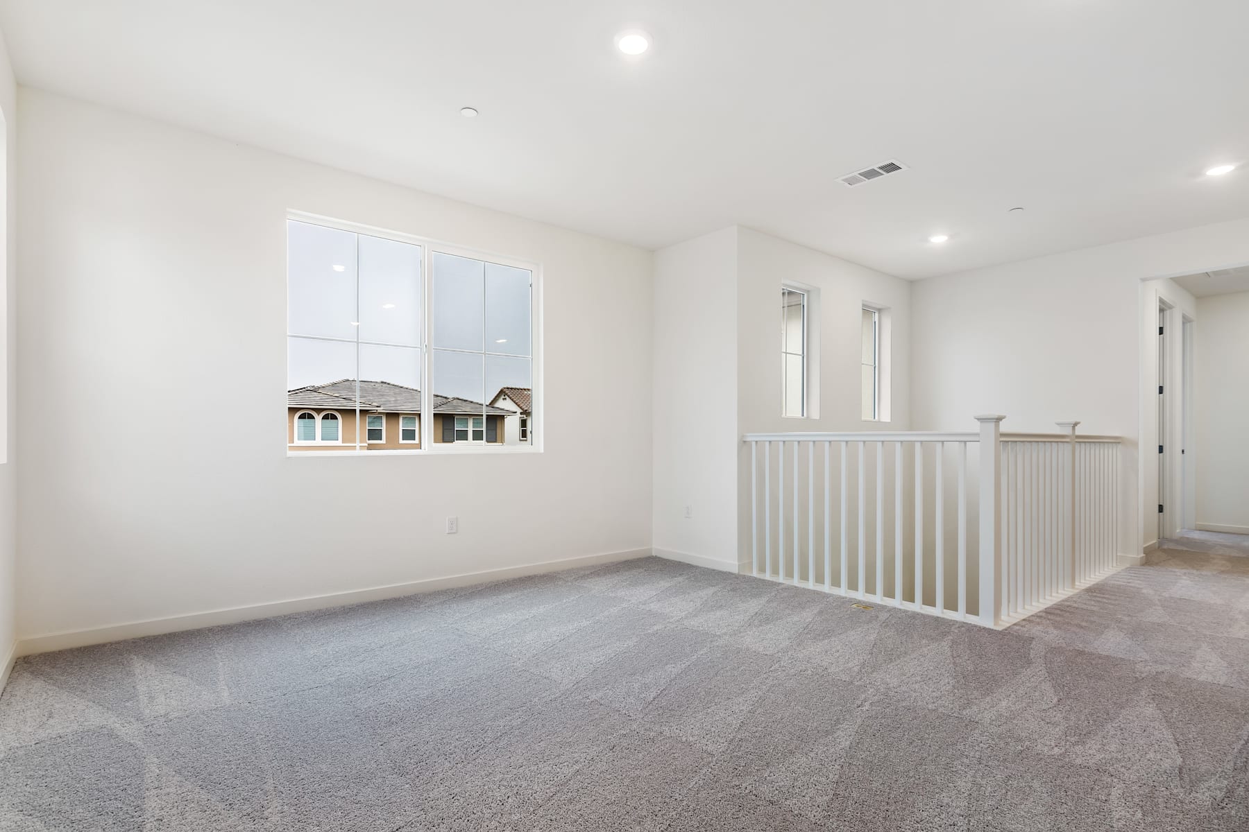 A spacious, well-lit room with a white wall, a wooden railing, and a view of the exterior through a large window.