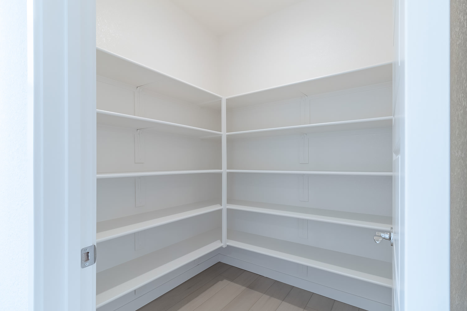 A corner of a room with white shelves and a wooden floor.