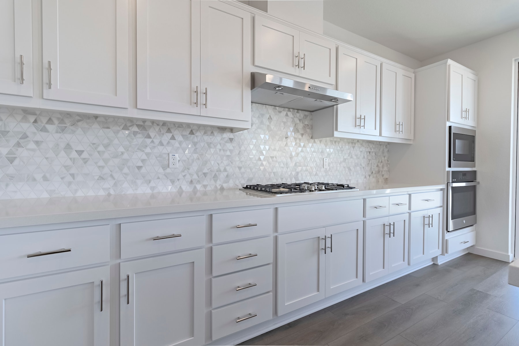 A modern, white kitchen with sleek cabinets, a tiled backsplash, and stainless steel appliances.