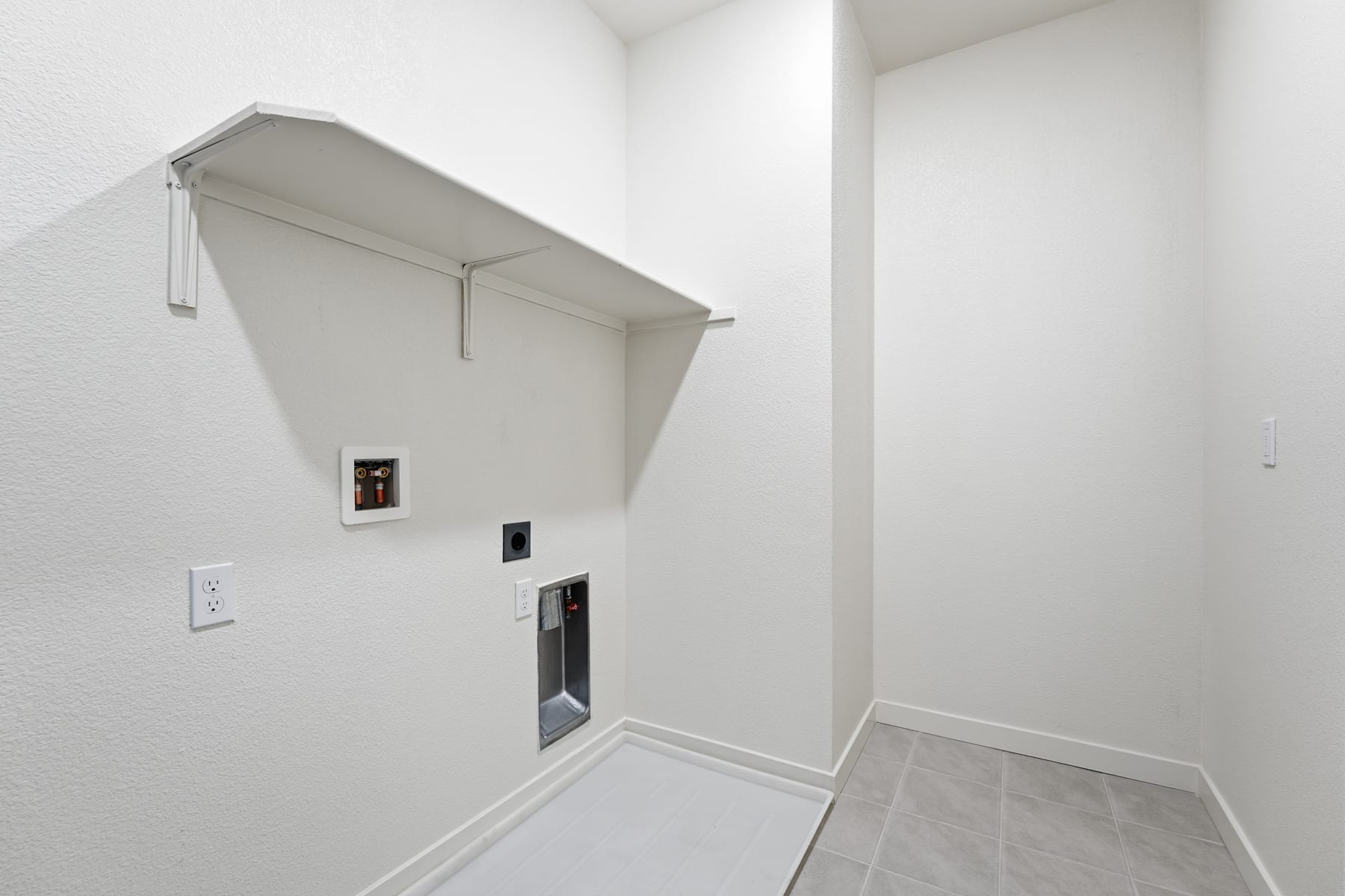 A white, minimalist hallway with a recessed shelf and electrical outlets on the wall.