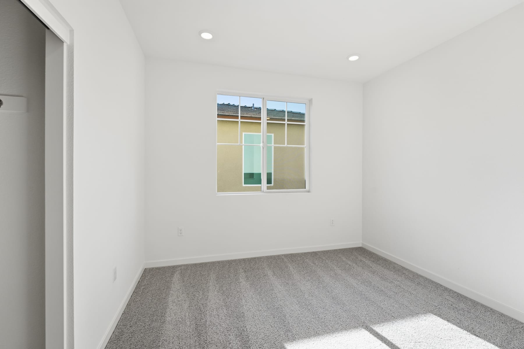 A simple, minimalist room with a large window featuring a stained glass design, providing natural light and a touch of color to the otherwise plain white walls and gray flooring.