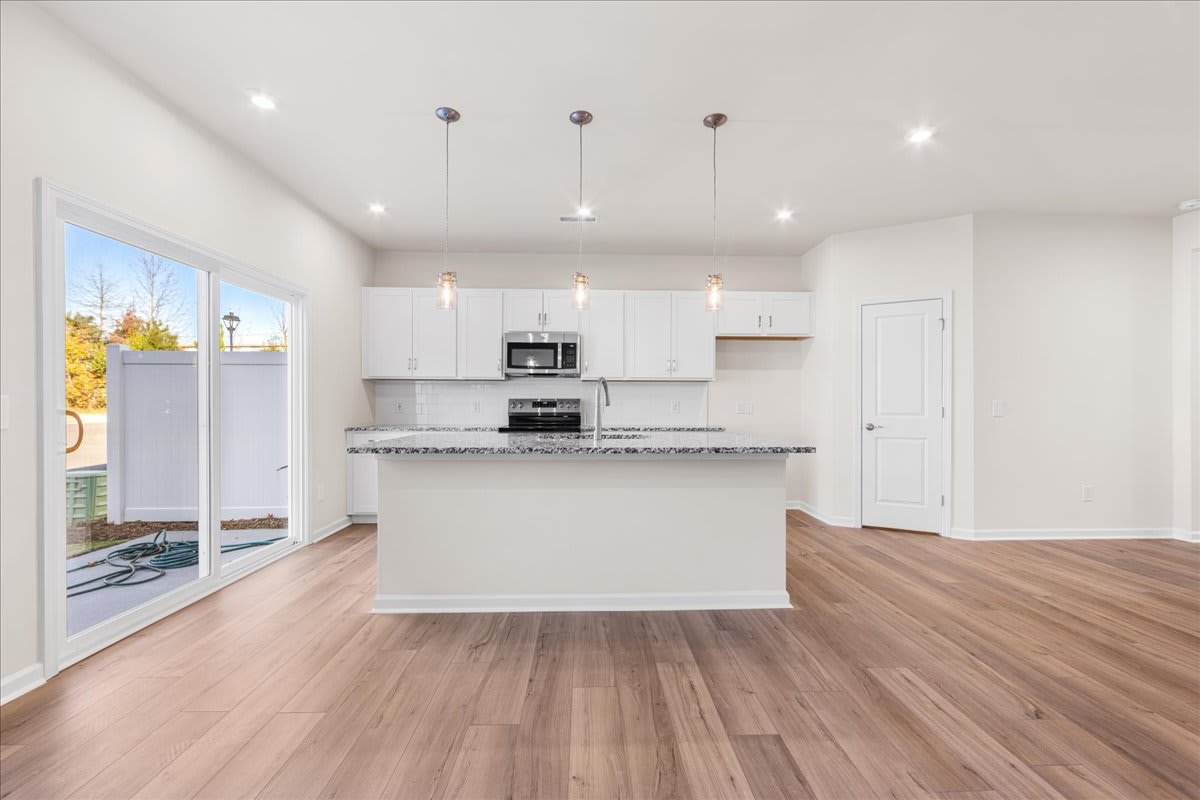 A modern, open-concept kitchen with white cabinets, stainless steel appliances, and a large window overlooking a scenic outdoor area.