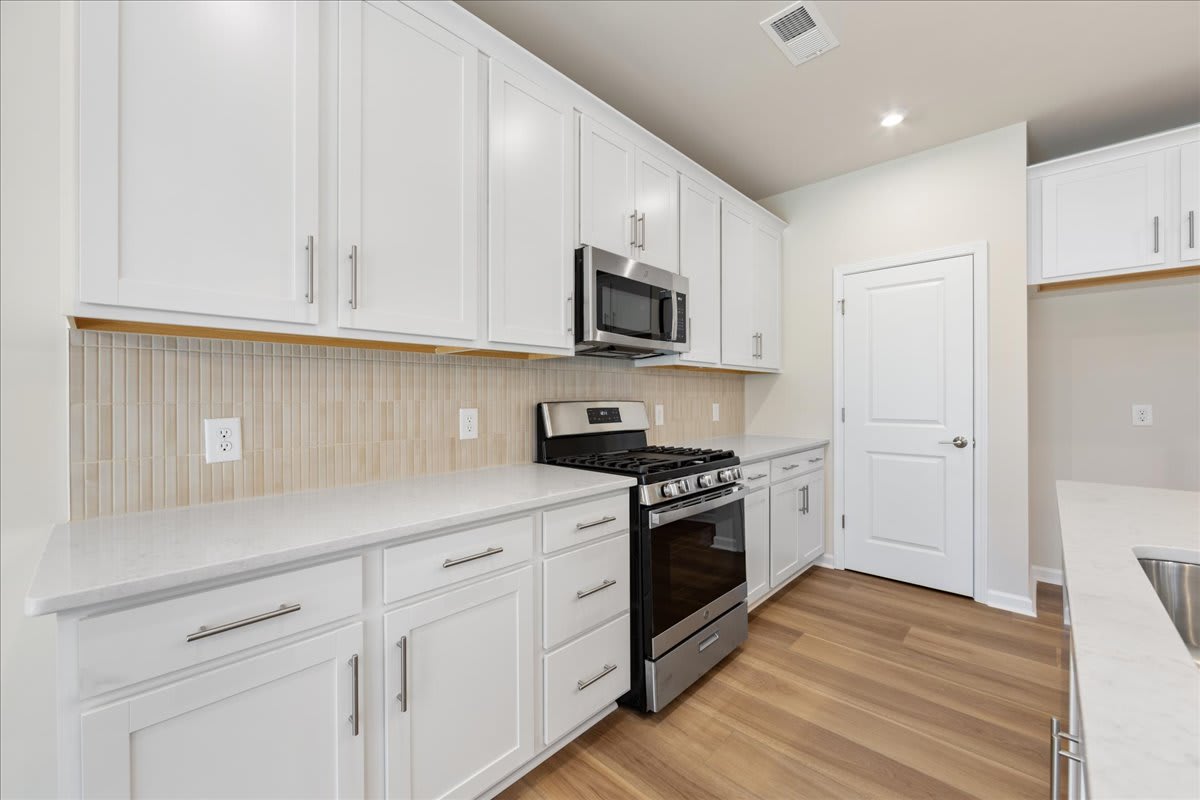 A modern, well-equipped kitchen with white cabinets, stainless steel appliances, and a wooden floor.