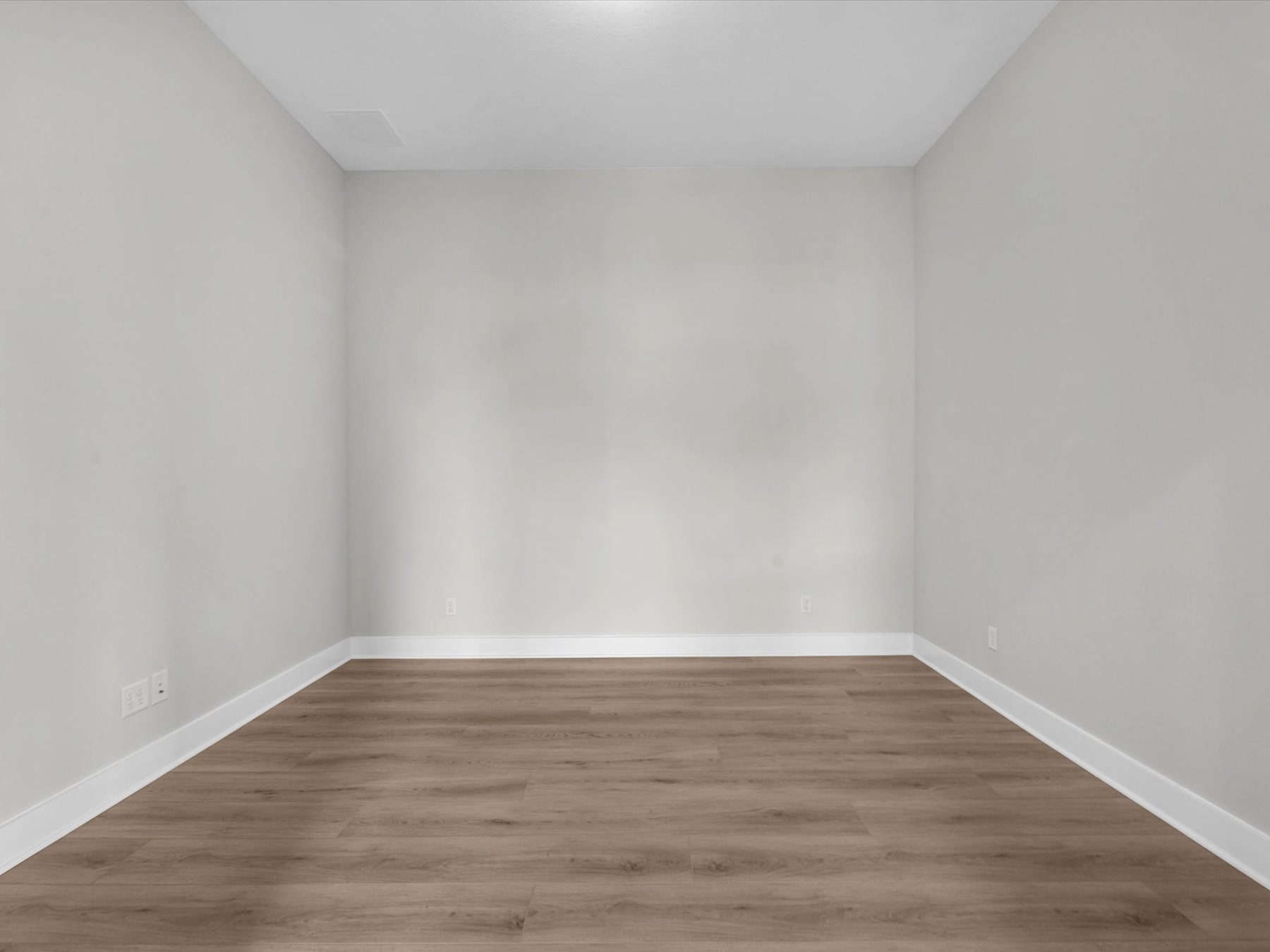 An empty room with white walls and a wooden floor, creating a minimalist and clean-looking space.