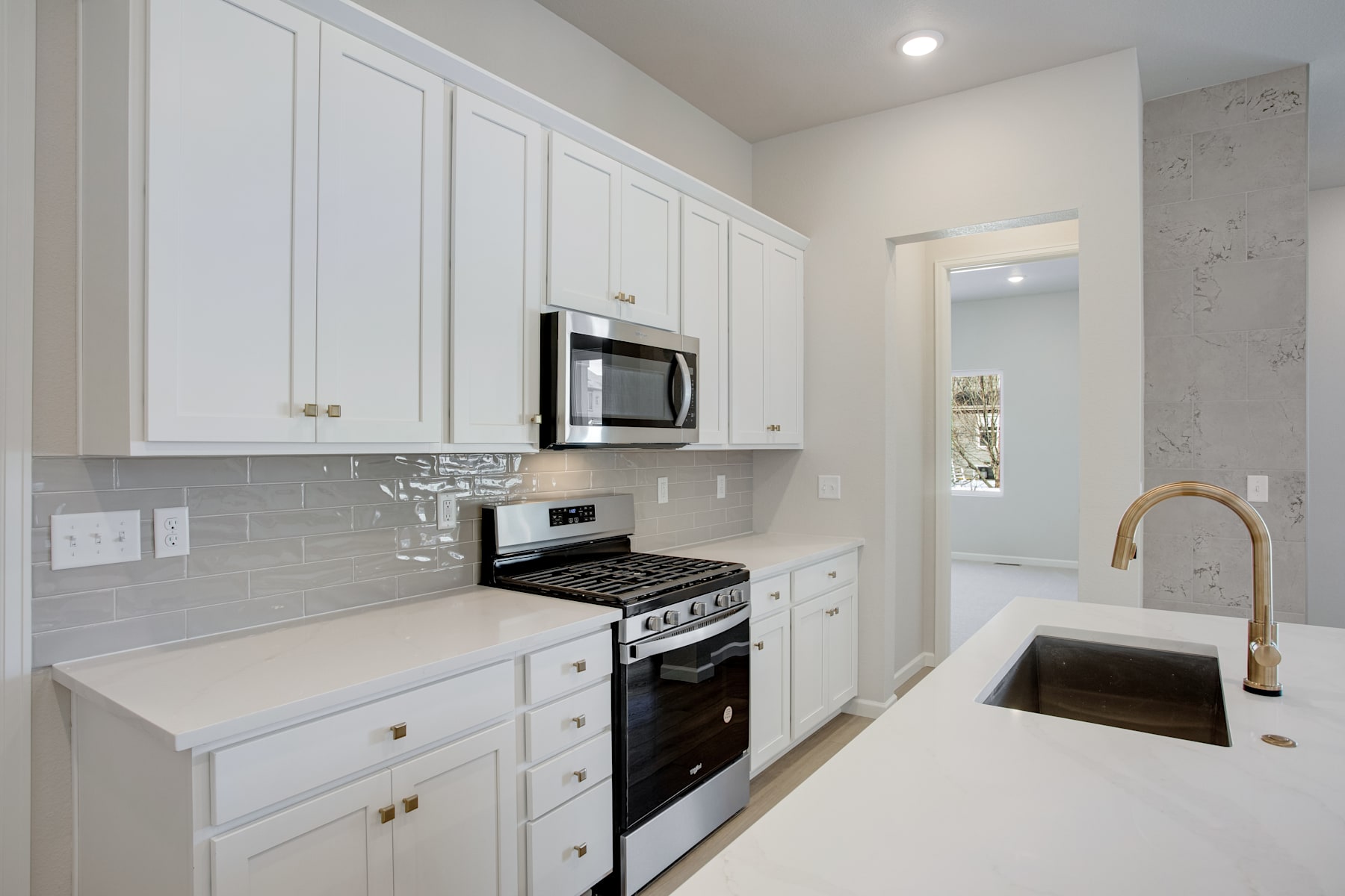 A modern, well-equipped kitchen with white cabinets, a stainless steel oven and microwave, and a white countertop with a sink and faucet.