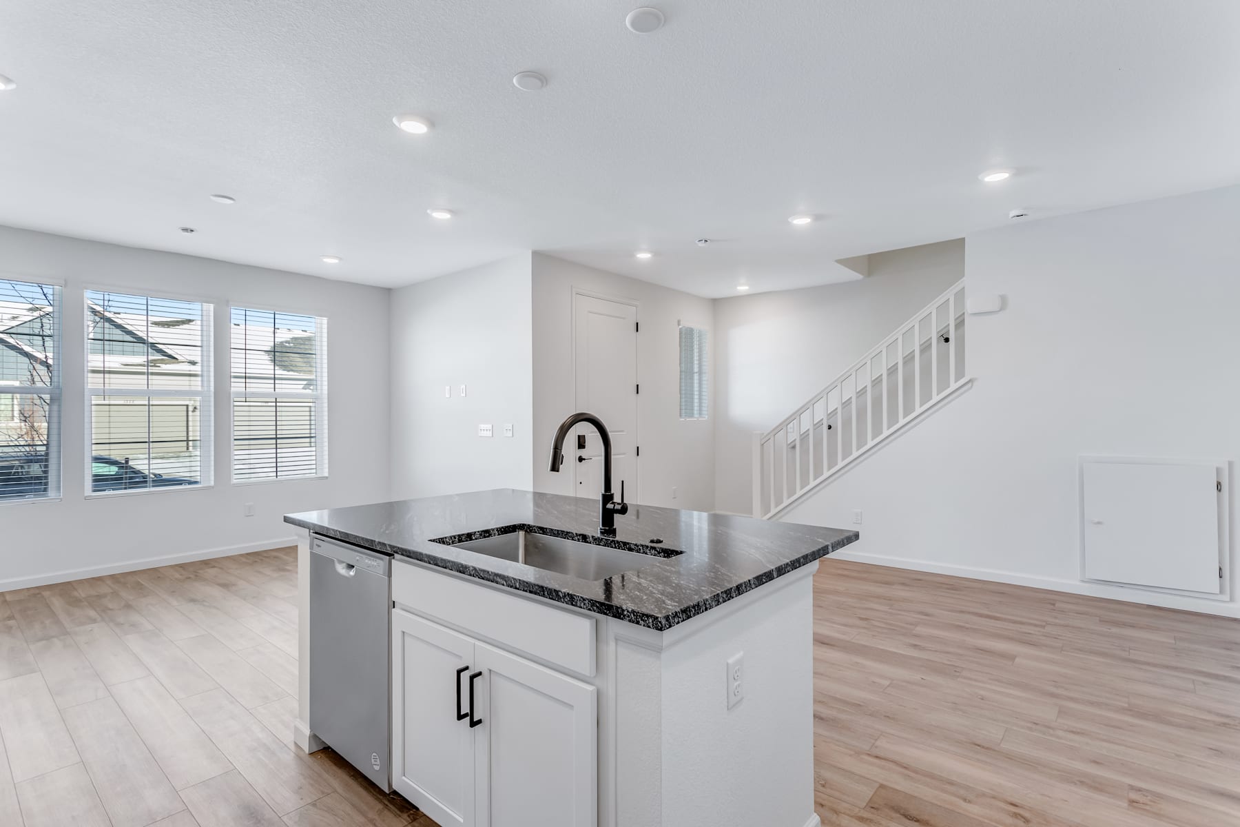 A modern, open-concept kitchen with a granite countertop island, white cabinets, and hardwood flooring, situated in a bright and airy living space with large windows.