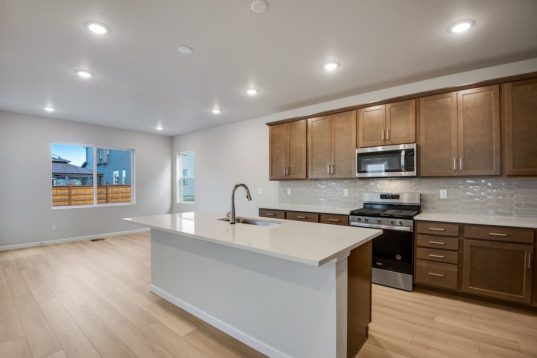 A modern and spacious kitchen with wooden cabinets, a white countertop, and stainless steel appliances, set against a bright and airy background.
