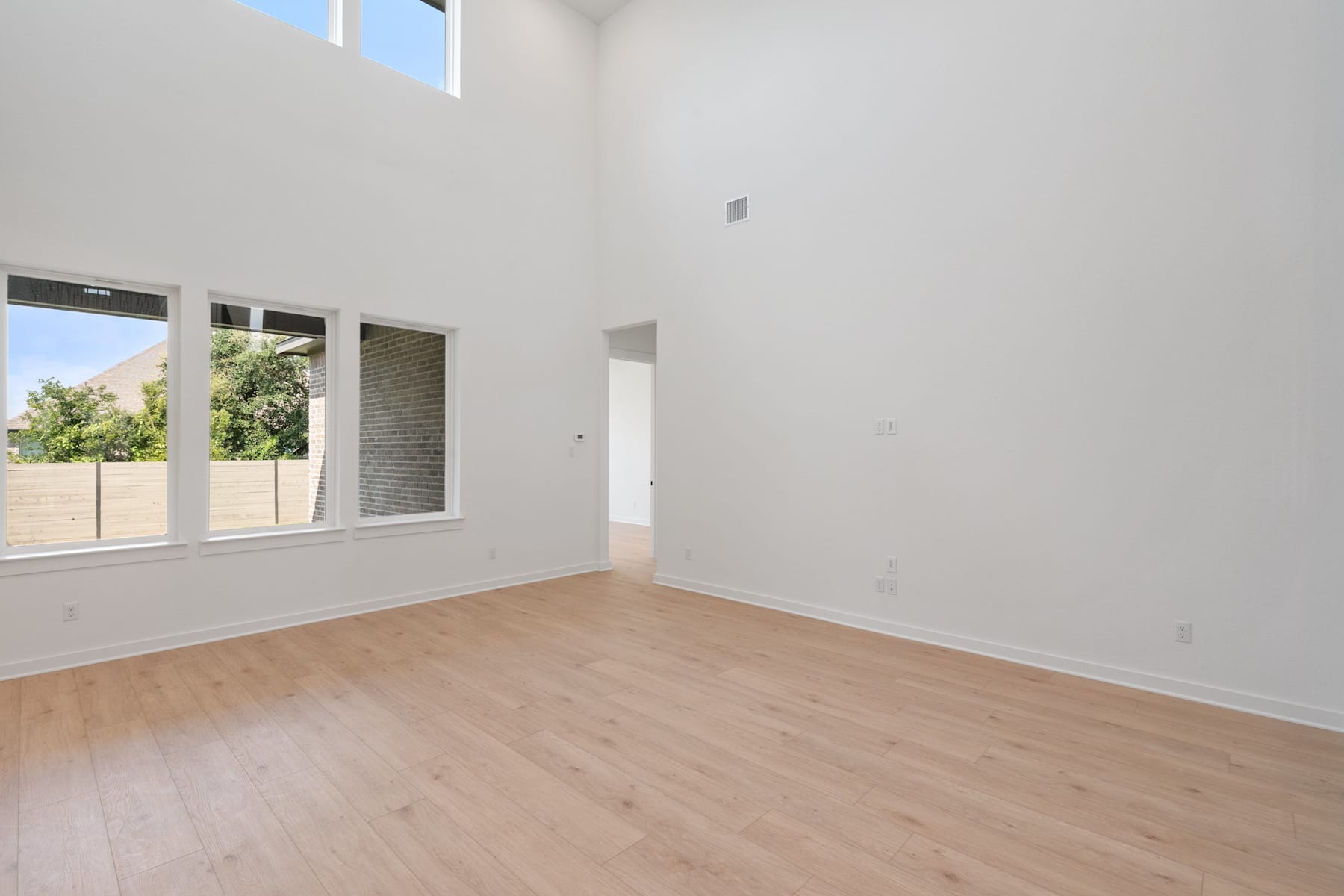 A spacious, bright room with large windows, white walls, and a wooden floor.